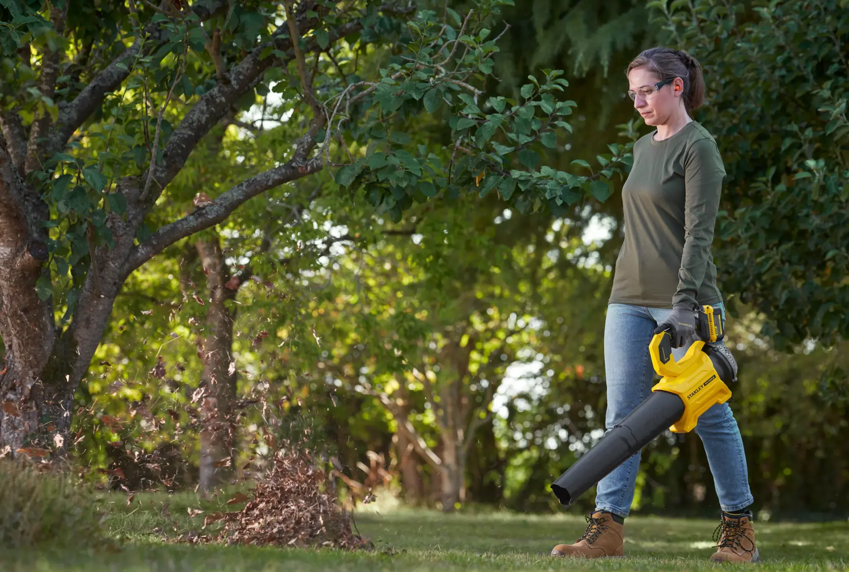 STANLEY SFMCBL730B Laubbläser im Außeneinsatz, gelb-schwarzes Design, bläst Blätter unter einem Baum.