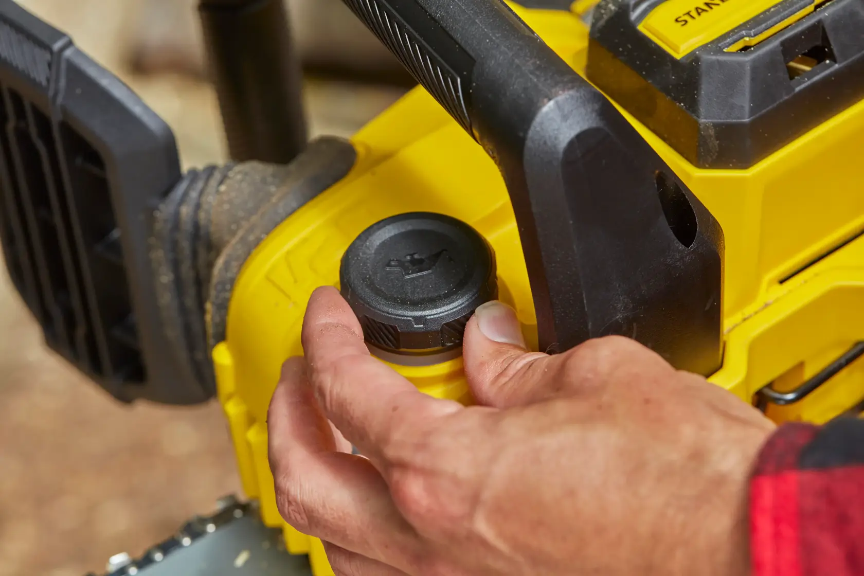STANLEY SFMCCS630B chainsaw close-up with hand adjusting oil cap, yellow and black design.