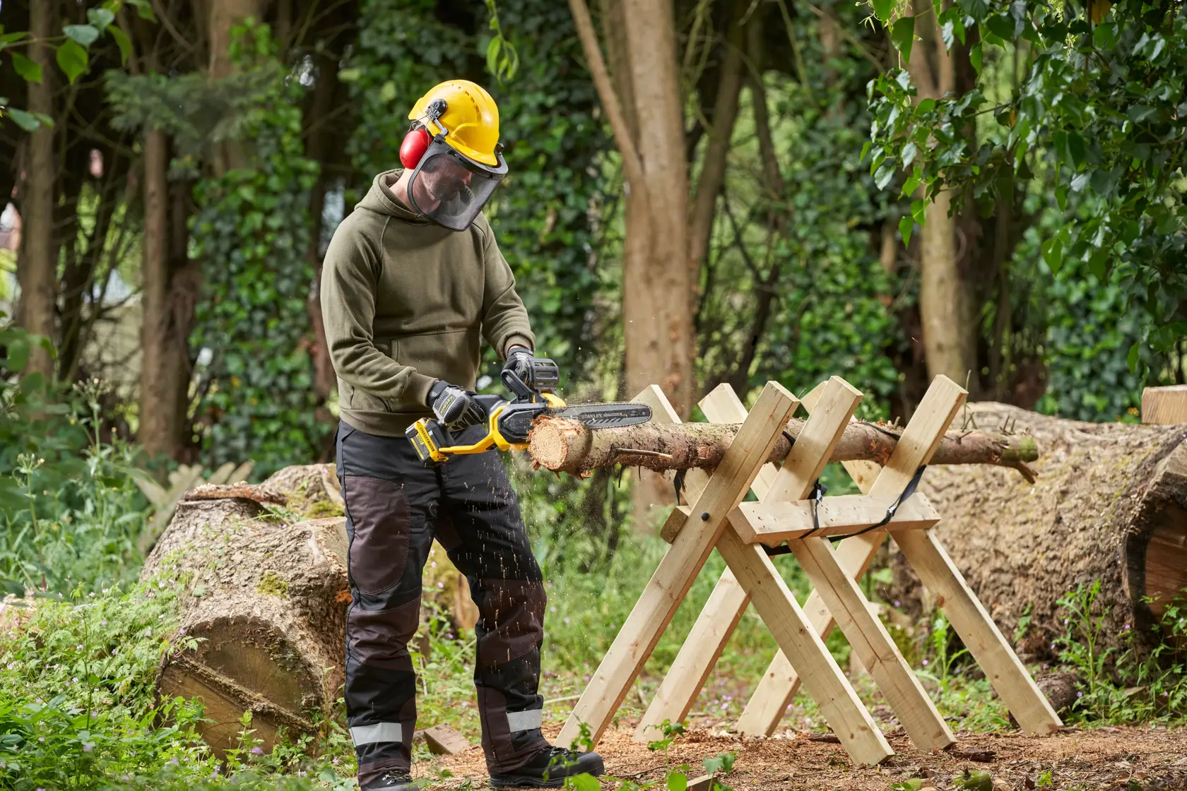 STANLEY SFMCCS730B Kettensäge schneidet Holzstamm im Freien, Anwender mit Schutzausrüstung im Waldgebiet.