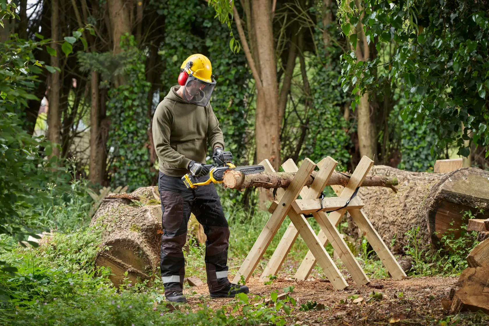 Foto einer Person, die mit der STANLEY SFMCCS730B Kettensäge Holz auf einer Sägebock im Freien schneidet.
