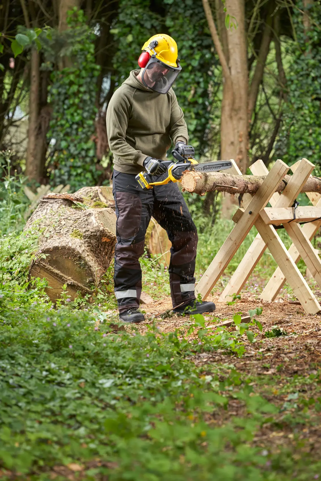 STANLEY SFMCCS730M1 Kettensäge im Einsatz im Freien zum Schneiden von Holz, gehalten von einer Person mit Schutzausrüstung.