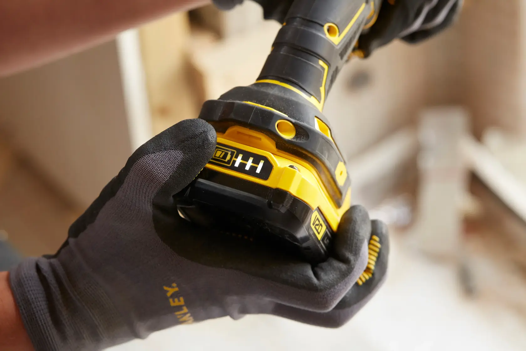 STANLEY SFMCD700C2K Akku-Bohrmaschine Nahaufnahme, behandschuhte Hand hält gelb-schwarzes Gerät, Batterieanzeige sichtbar.