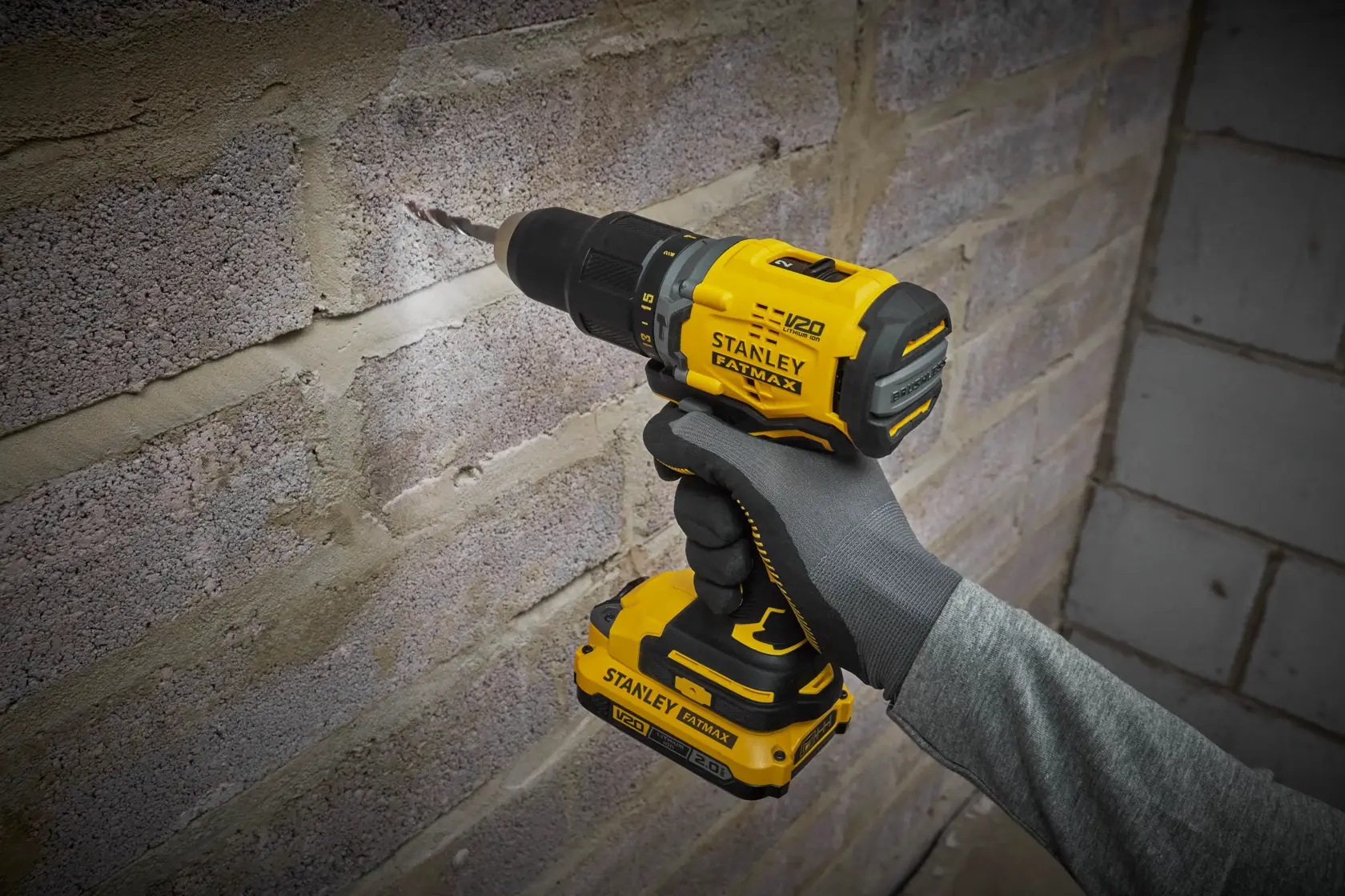 STANLEY SFMCD715D2K Akku-Bohrmaschine im Einsatz beim Bohren einer Ziegelwand, Nahaufnahme seitlich.