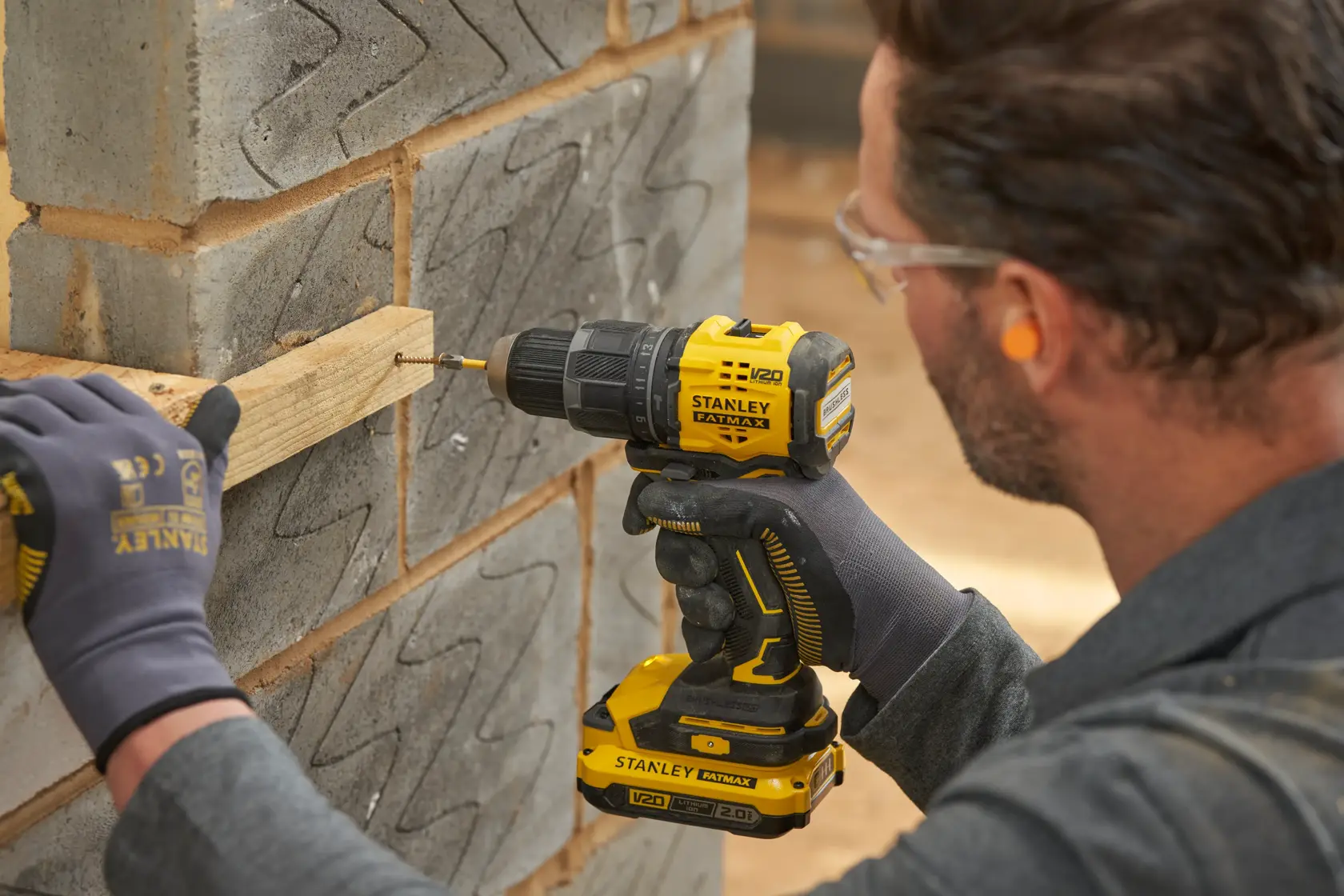 STANLEY SFMCD716B-XJ Akku-Bohrmaschine beim Eindrehen einer Schraube in Holz an einer Betonwand.