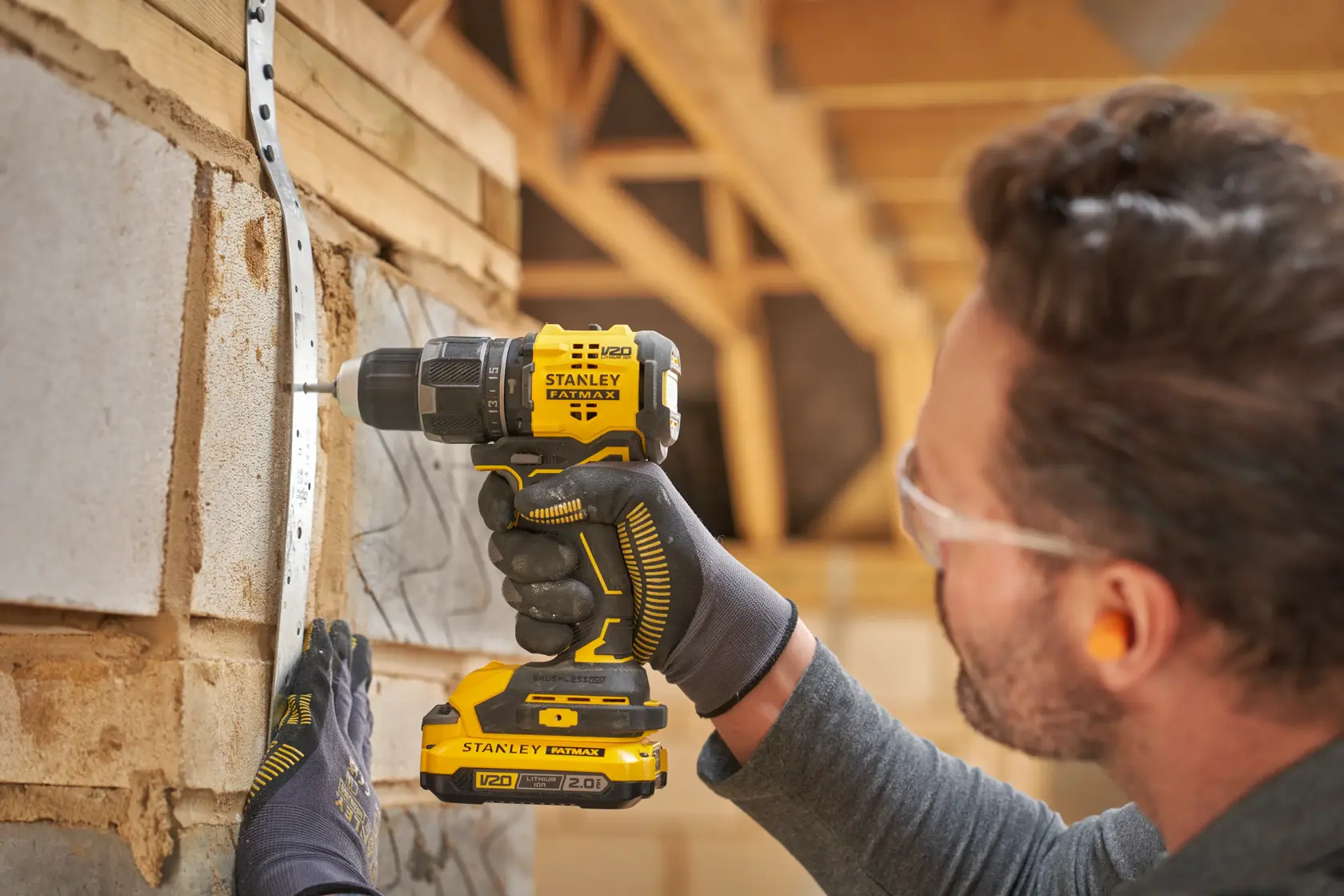 STANLEY SFMCD716B-XJ Akku-Bohrmaschine in Benutzung, Seitenansicht, Bohren in die Wand mit V20-Akku, Mann mit Handschuhen.
