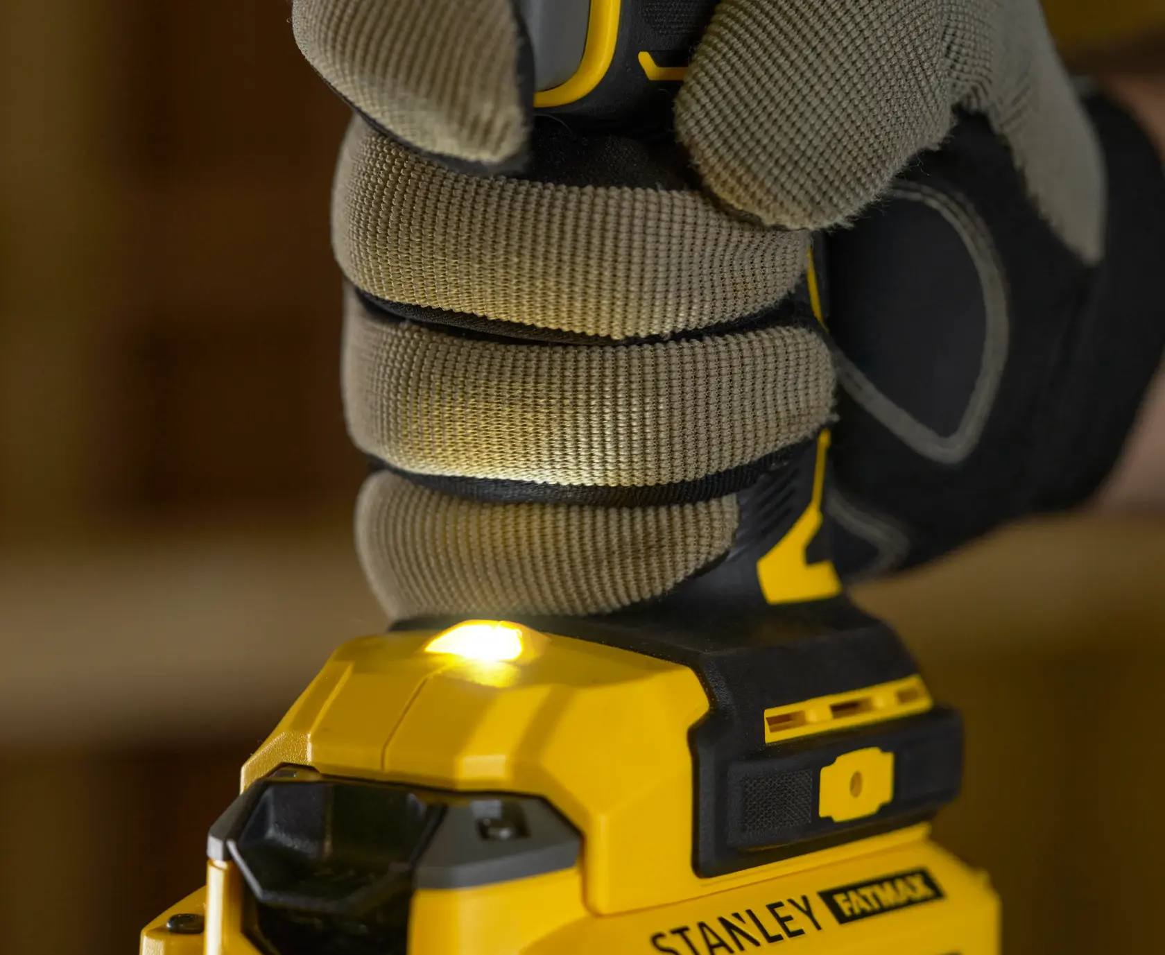 Photo of gloved hand gripping STANLEY SFMCD720D2K cordless drill with LED light on, close-up view.