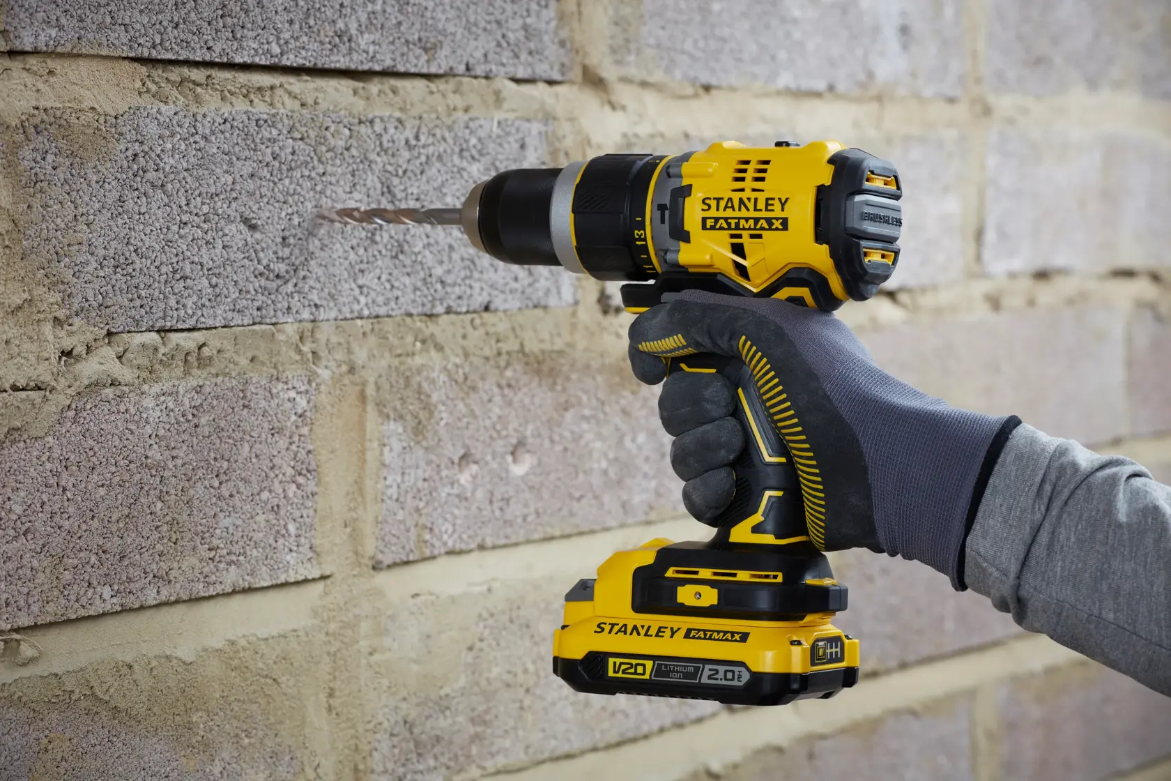 Photo of STANLEY SFMCD721D2K cordless drill in use on brick wall, yellow and black design, side angle.