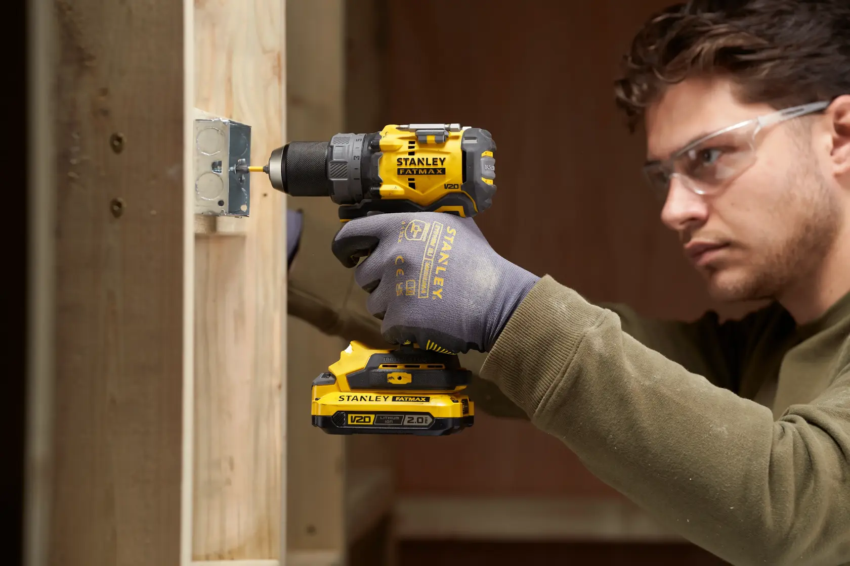 Foto des kabellosen STANLEY SFMCD725D2K Bohrschraubers im Einsatz an Holzrahmen, Seitenansicht, Arbeiter mit Handschuhen.