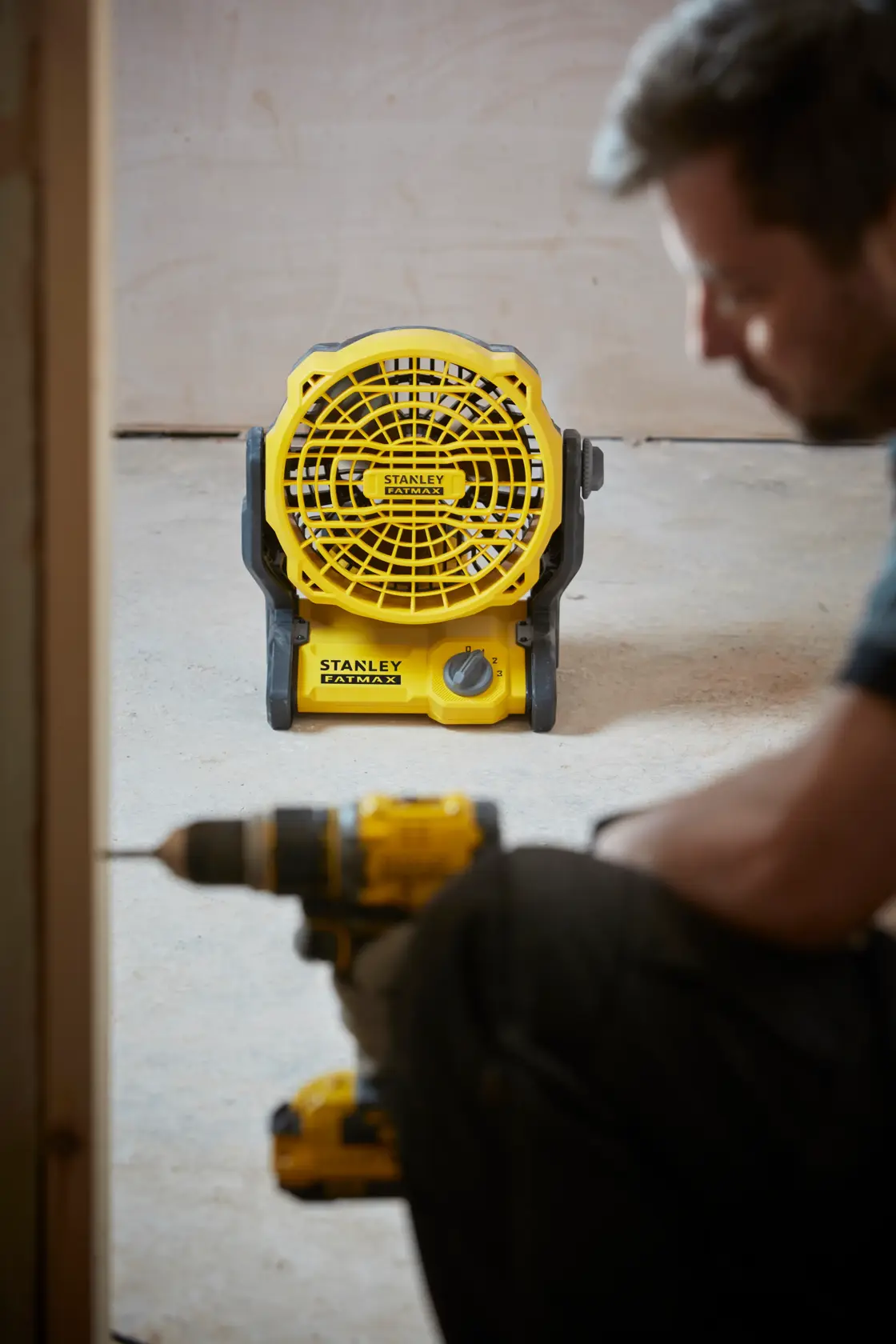 Photo of STANLEY SFMCE001B yellow portable fan on floor with construction tool in foreground.