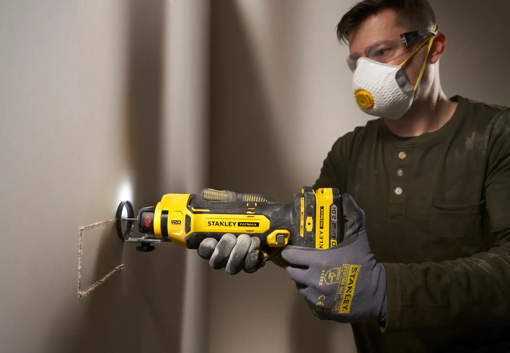 Foto des STANLEY SFMCE200B Rotationswerkzeugs beim Schneiden von Gipskarton, gehalten von behandschuhten Händen, Baustelle.