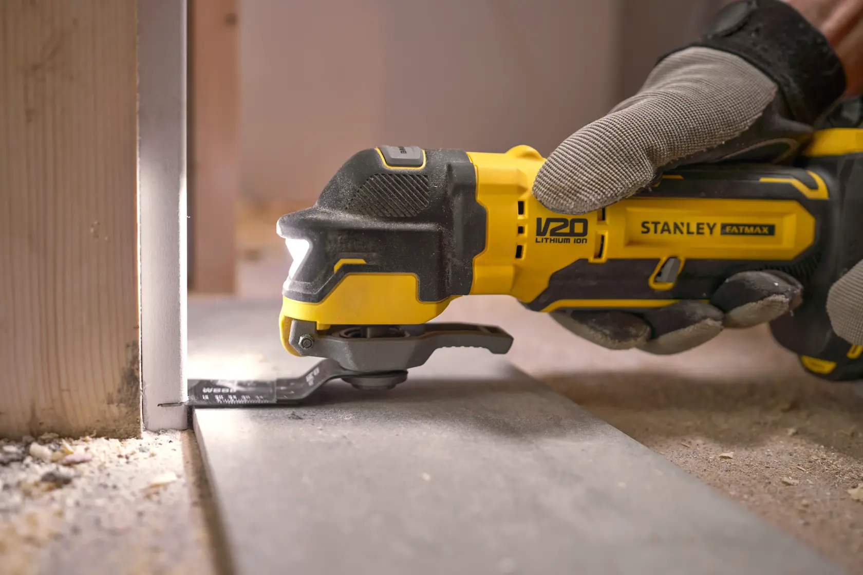 Stanley SFMCE510M2K oszillierendes Multifunktionswerkzeug schneidet Bodenplatte, Nahaufnahme mit Handschuh, Baustelle.