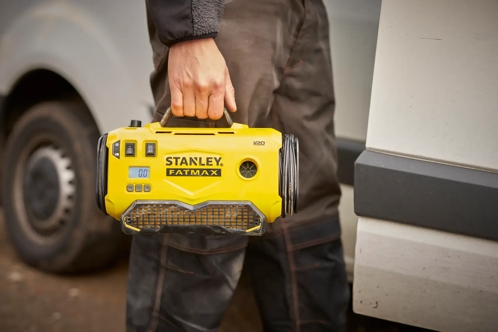 Stanley SFMCE520B tragbarer gelber Kompressor am Griff gehalten, draußen nahe einem Fahrzeug.