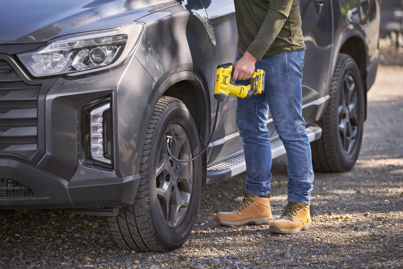 STANLEY SFMCE521B tragbarer Kompressor beim Aufpumpen eines Autoreifens im Freien.