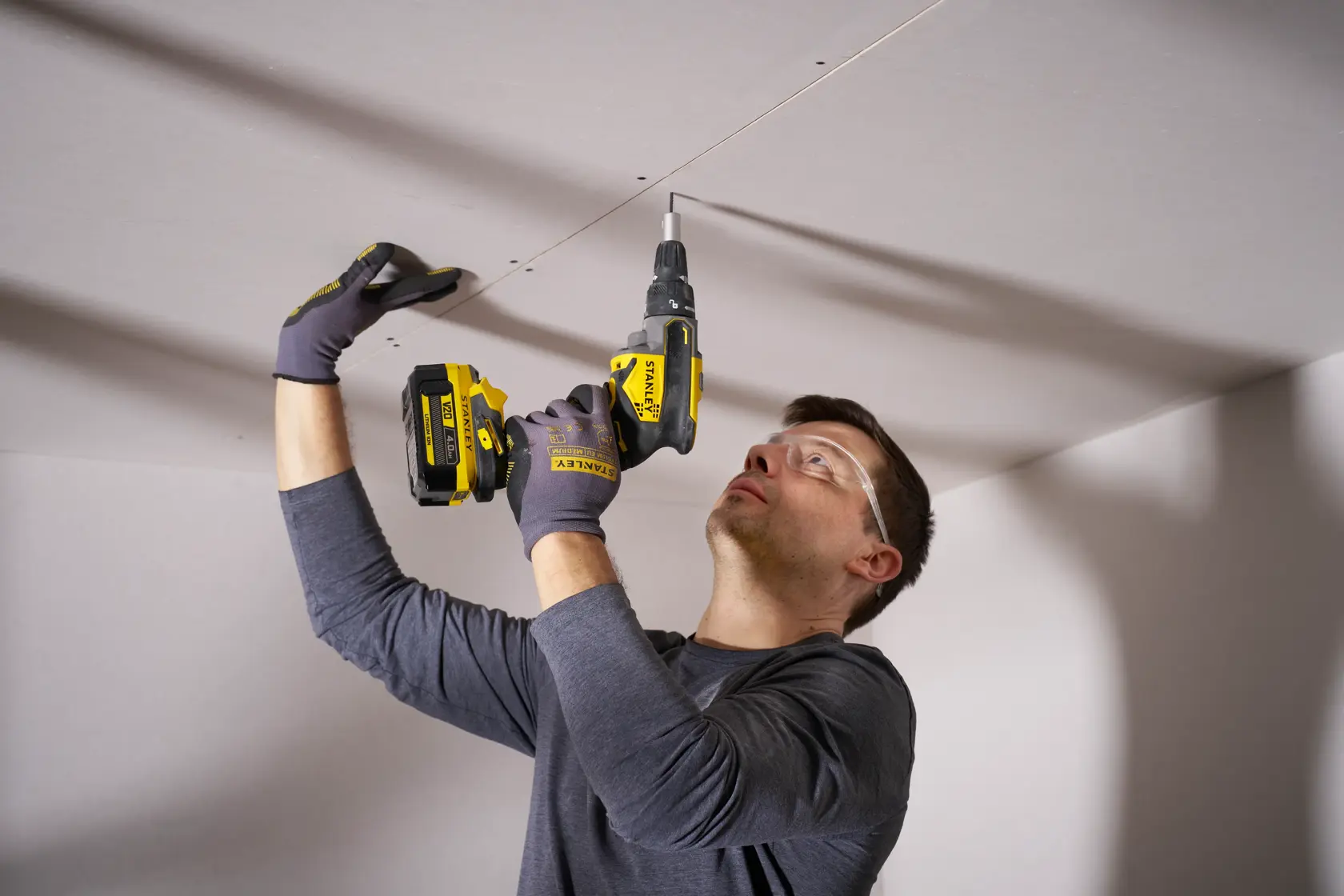 STANLEY SFMCF600B Schlagschrauber beim Verschrauben von Trockenbauplatten an der Decke, Nahaufnahme im Innenbereich.