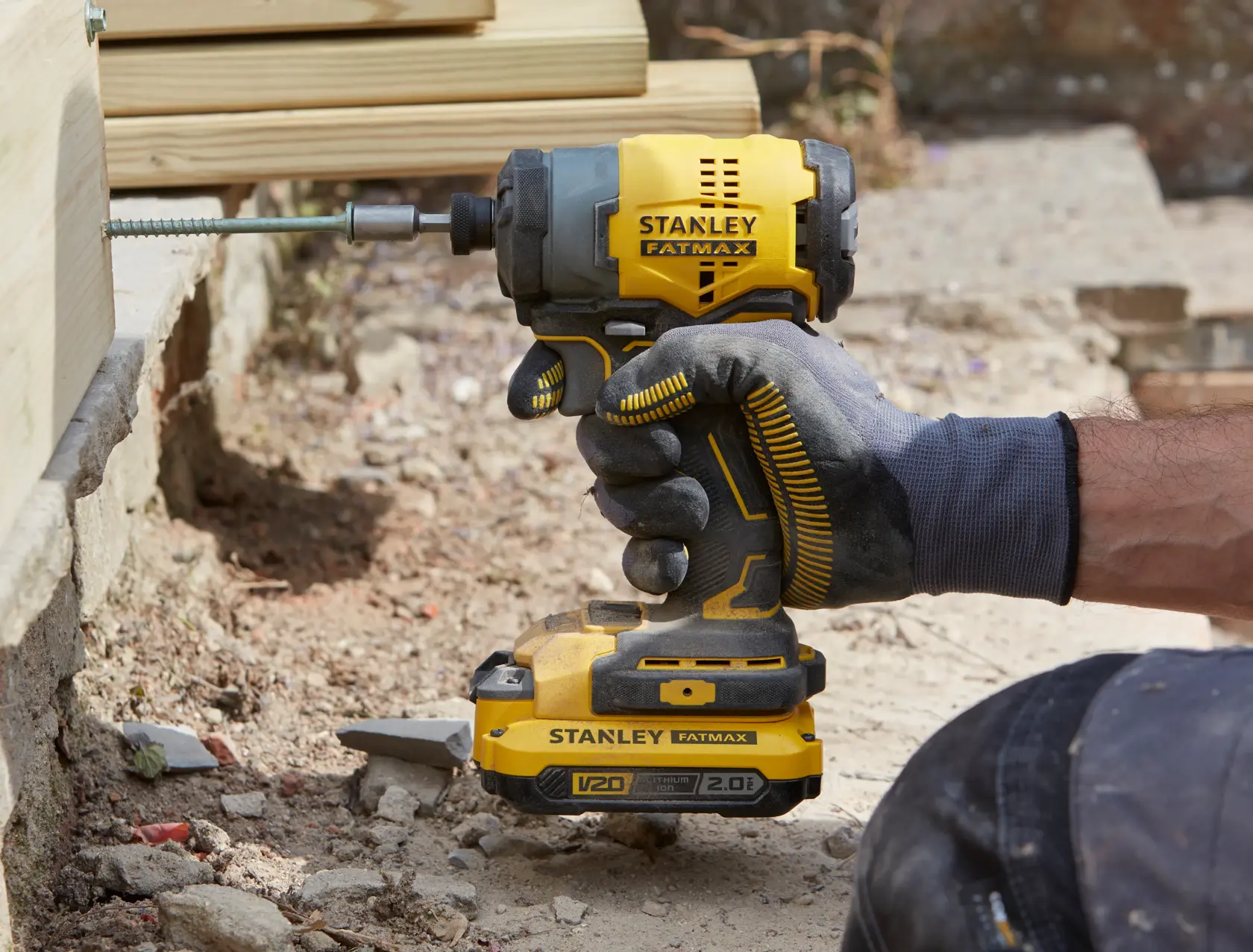 Stanley SFMCF810B Schlagschrauber von behandschuhter Hand gehalten, Schraube in Holz, Outdoor-Baustelle.