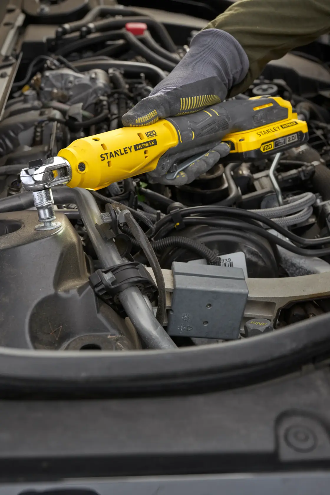 Foto des kabellosen Ratschenwerkzeugs STANLEY SFMCF930B im Einsatz an einem Automotor durch eine behandschuhte Hand.