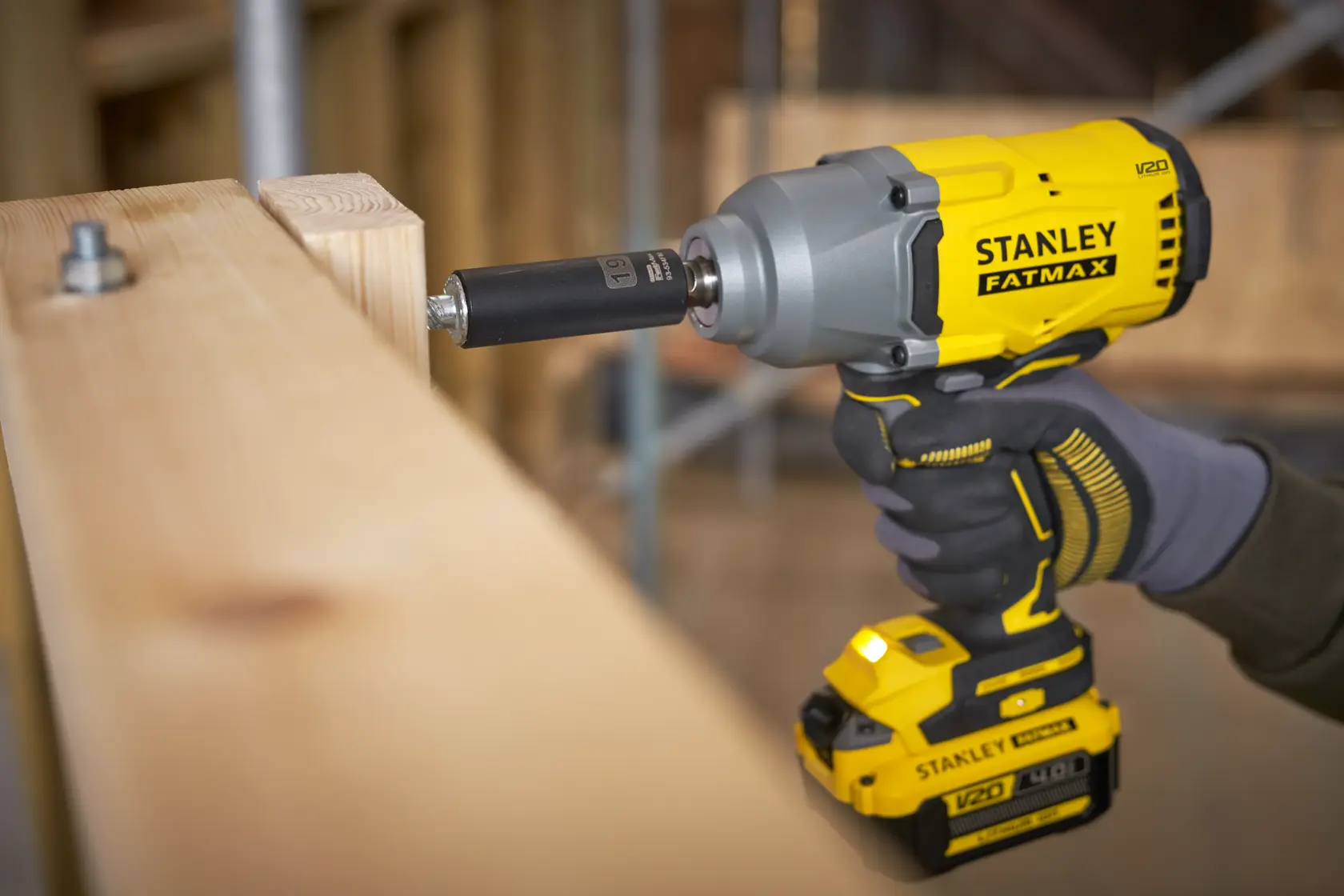 Photo of STANLEY SFMCF940B cordless impact wrench in use, driving a bolt into wooden beams.