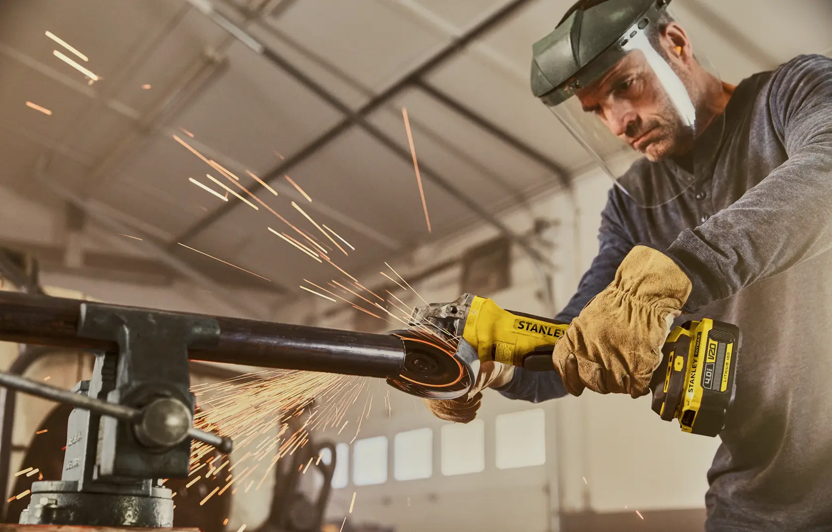 STANLEY SFMCG700M2K cordless angle grinder in use, sparks flying, worker wearing gloves and face shield.