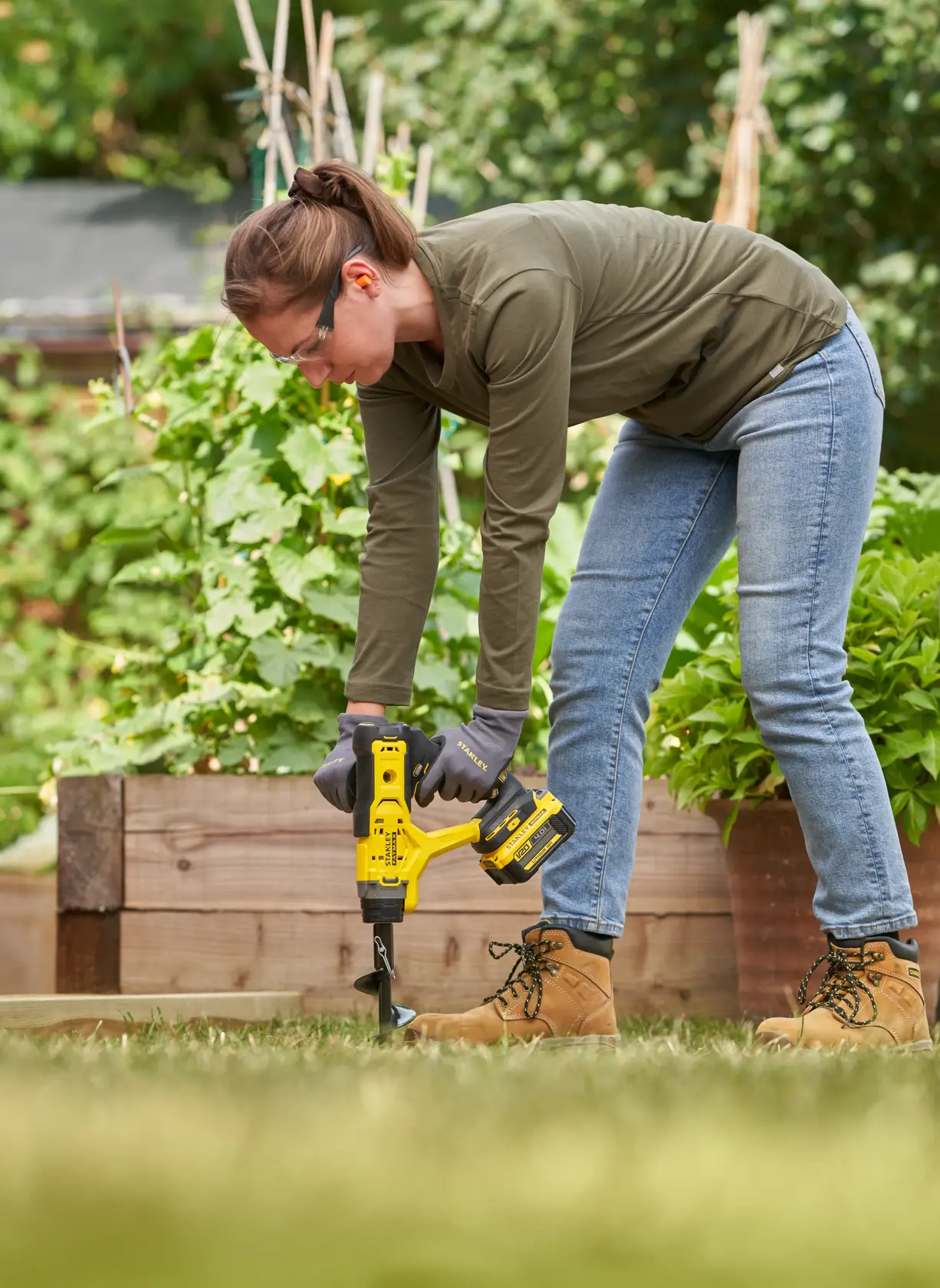 STANLEY SFMCGA75M1 cordless garden auger in use outdoors near raised garden beds.