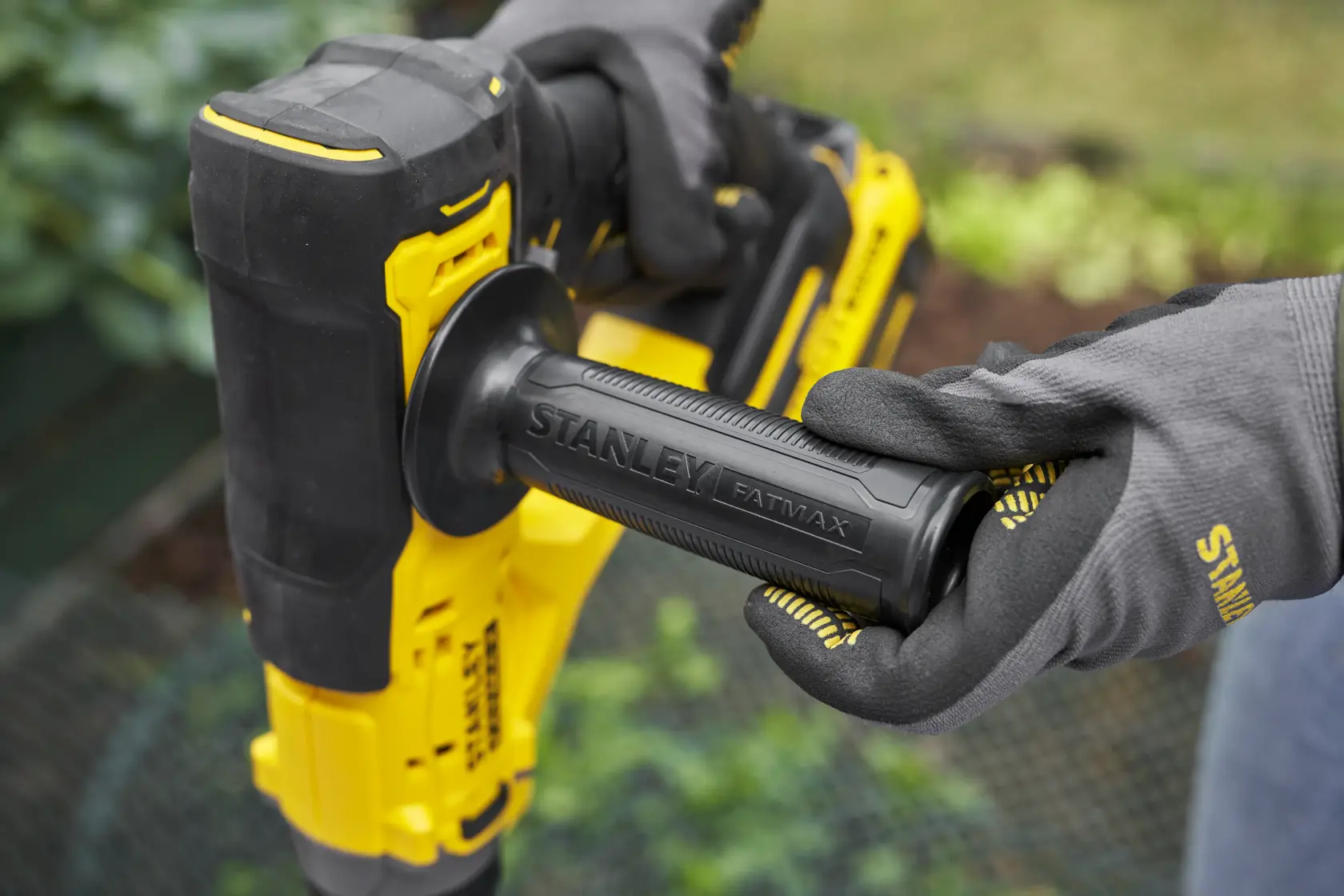 Photo of STANLEY SFMCGA75M1 yellow and black power tool handle held by gloved hands, outdoor setting.