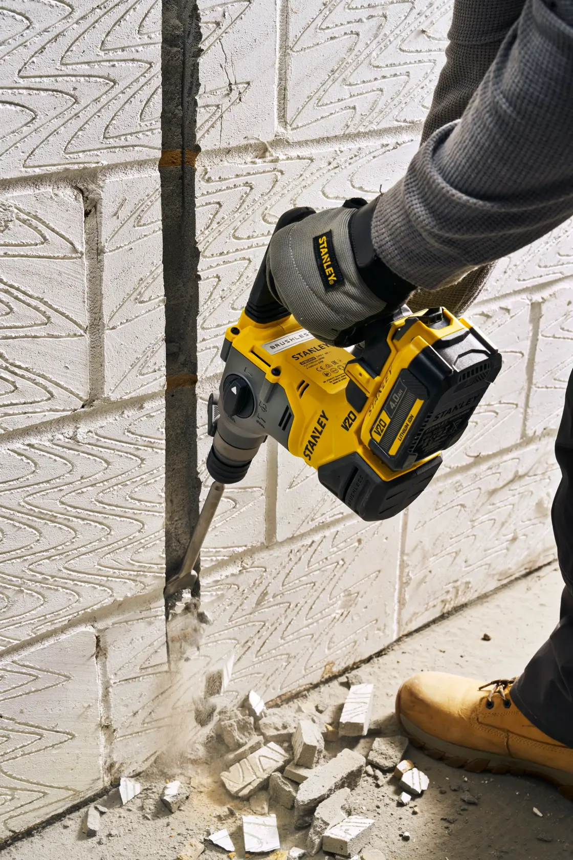 Foto vom STANLEY SFMCH910M1T Bohrhammer im Einsatz beim Stemmen einer Betonwand, Arbeiter mit Handschuhen und Stiefeln.