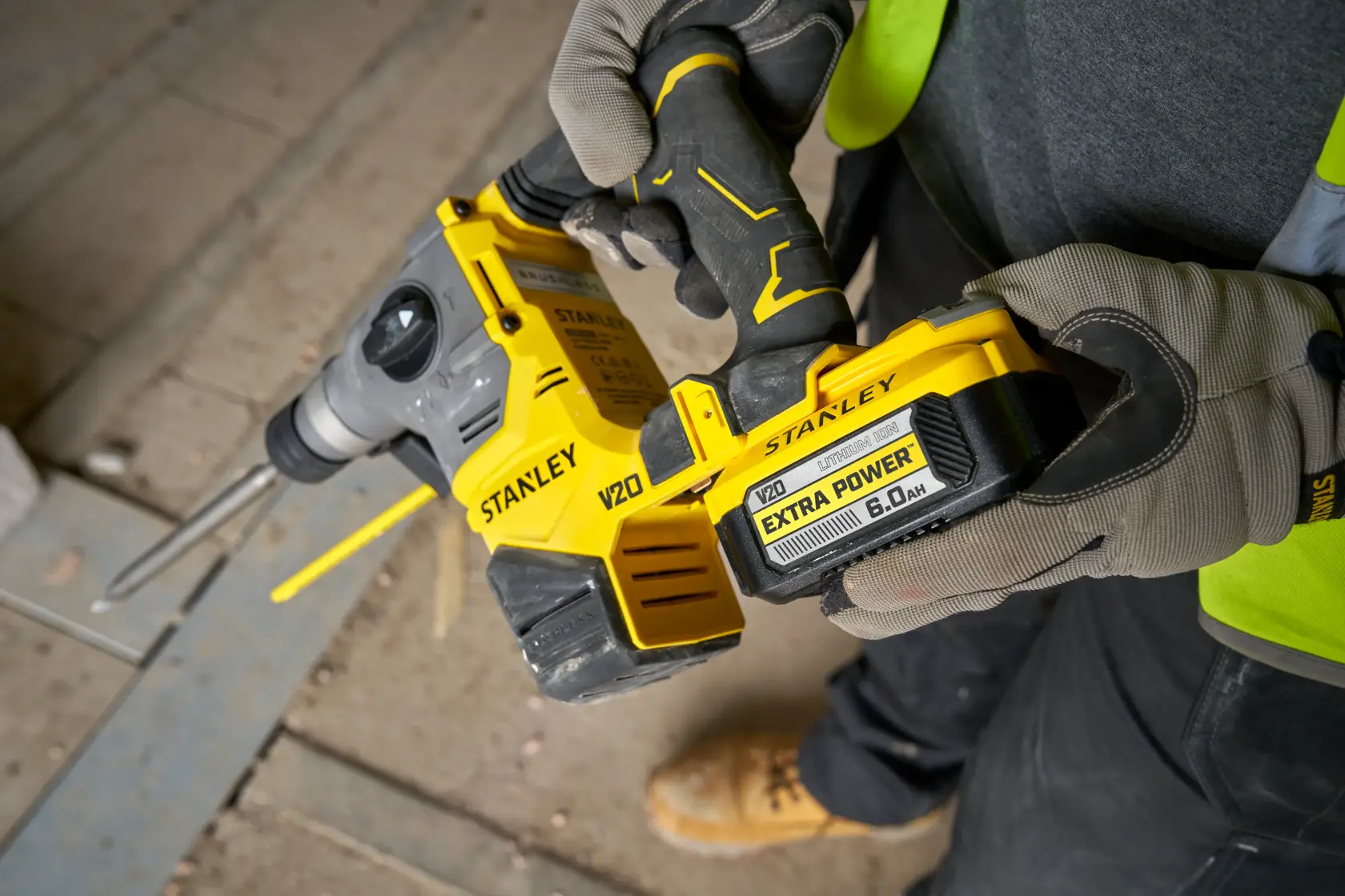 Stanley V20 Akku-Bohrhammer wird von einer Person mit Handschuhen auf einer Baustelle gehalten.