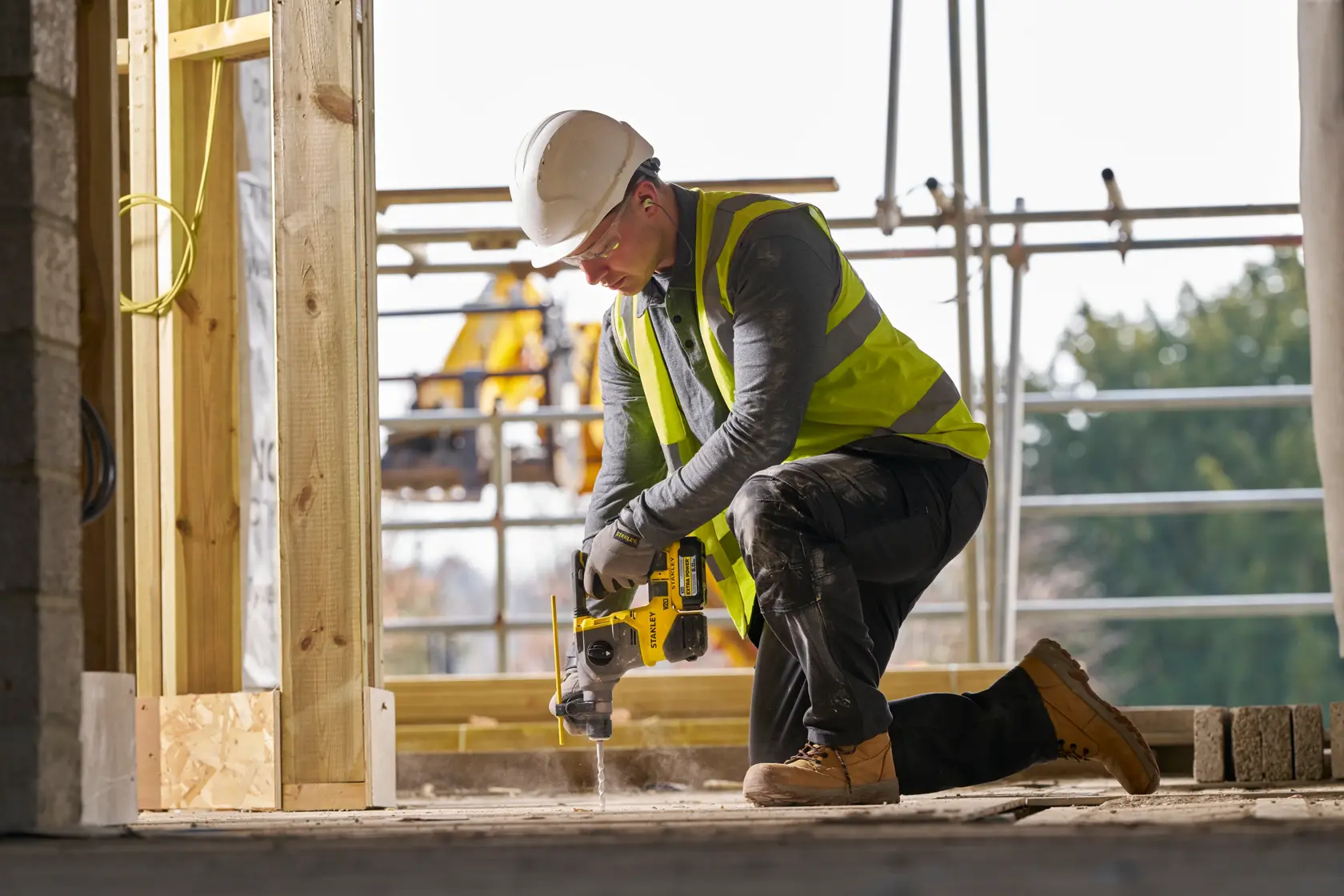Arbeiter mit Schutzausrüstung nutzt einen gelben Stanley-Bohrer auf Beton.