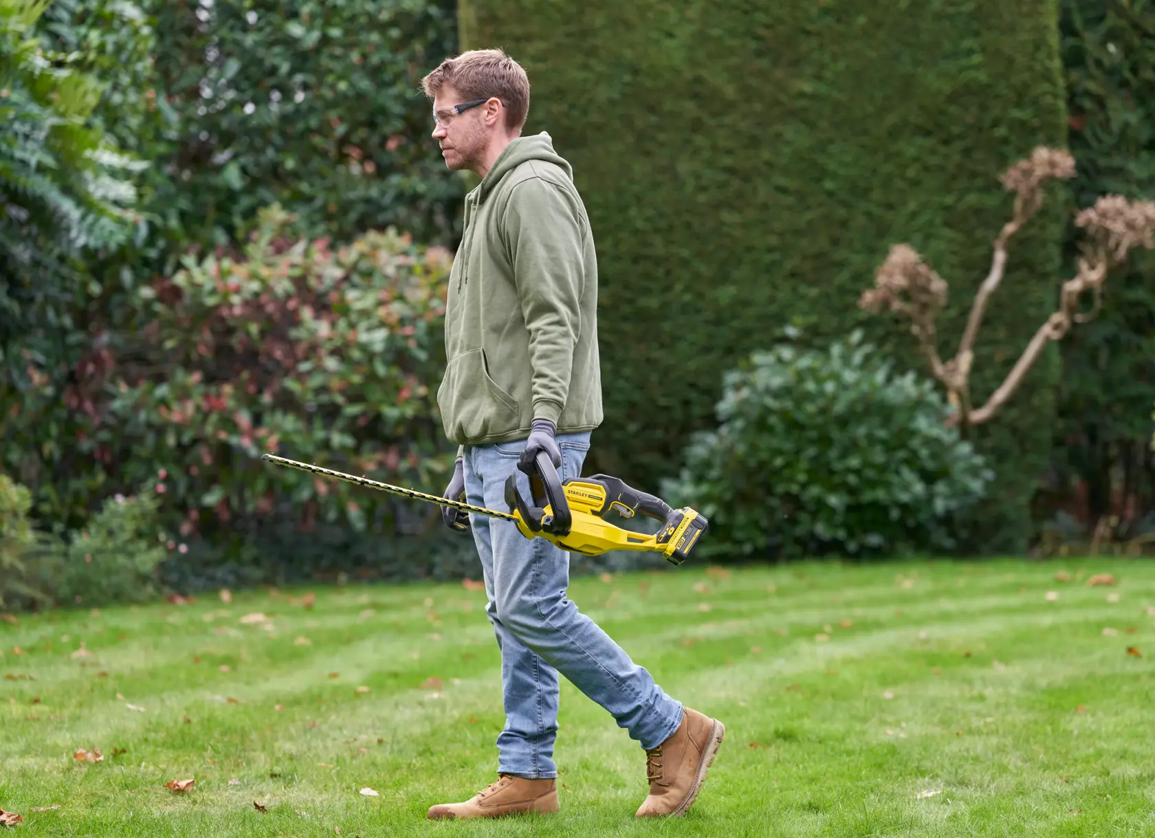 Foto des STANLEY SFMCHT655M1 Heckenschneiders, gehalten von Person im Garten, gelbes und schwarzes Design.