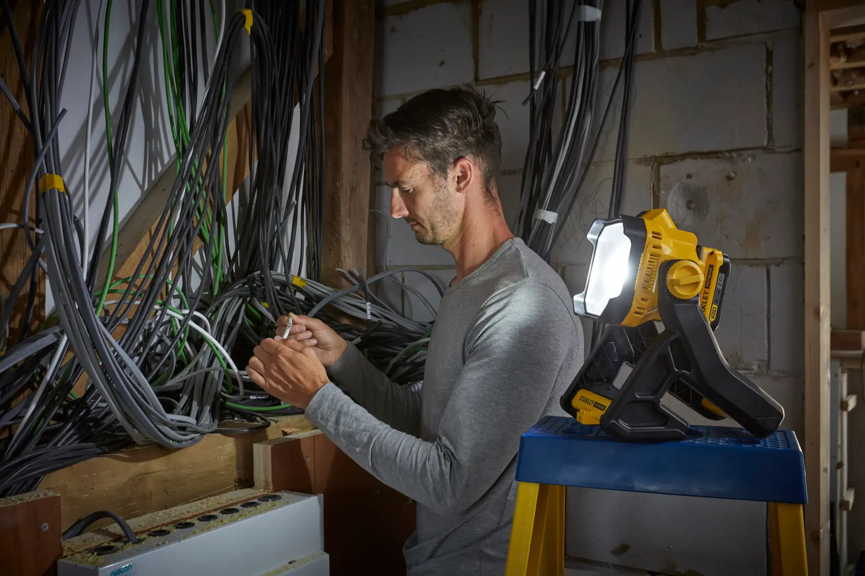 Stanley SFMCL030B Arbeitsleuchte beleuchtet Elektriker zwischen Kabeln an einer unfertigen Wand.