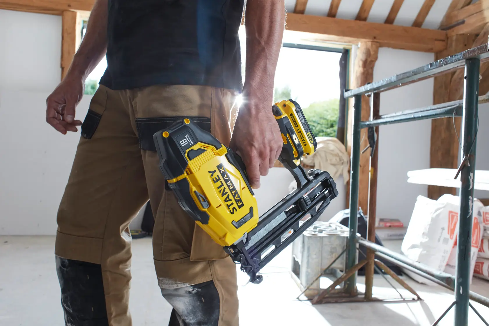 STANLEY SFMCN616D2K kabelloser Nagler in der Hand einer Person mit Arbeitshose auf Baustelle.