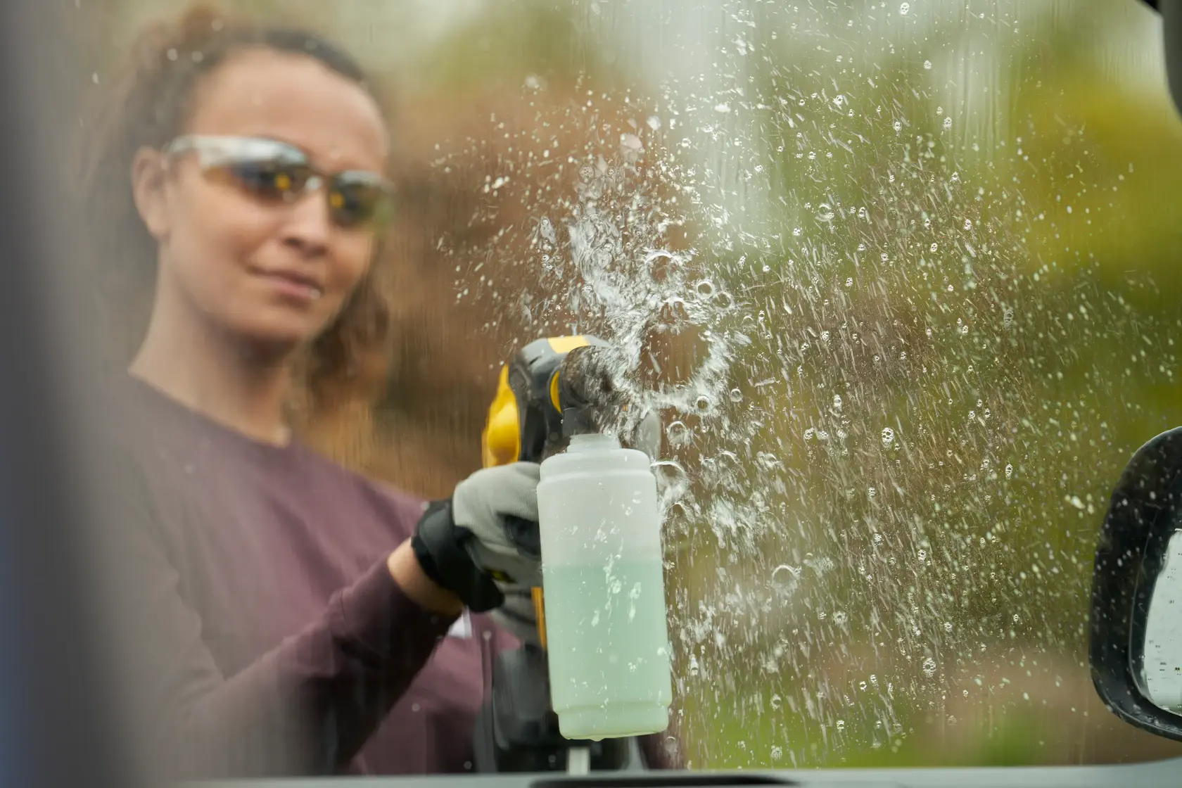 Photo of STANLEY SFMCPC93M1 cleaning tool spraying liquid onto a car window outdoors.