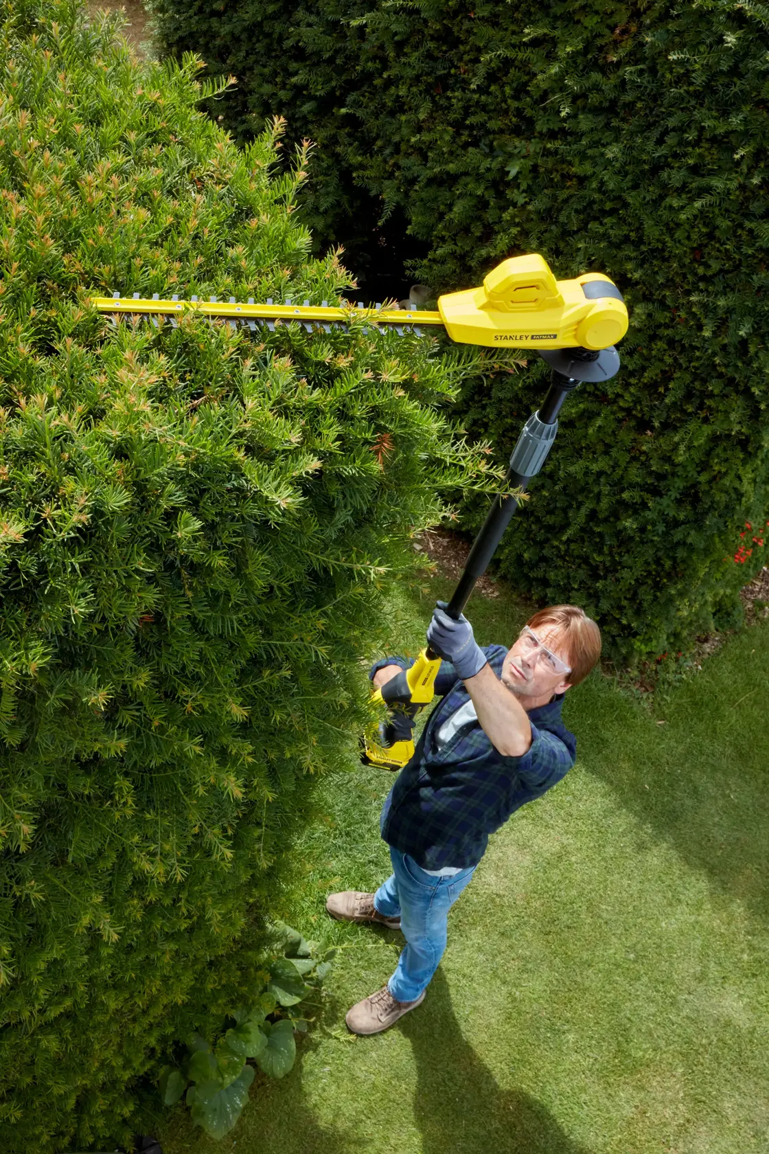 STANLEY SFMCPH845B photography of cordless pole hedge trimmer in use trimming tall green bushes.