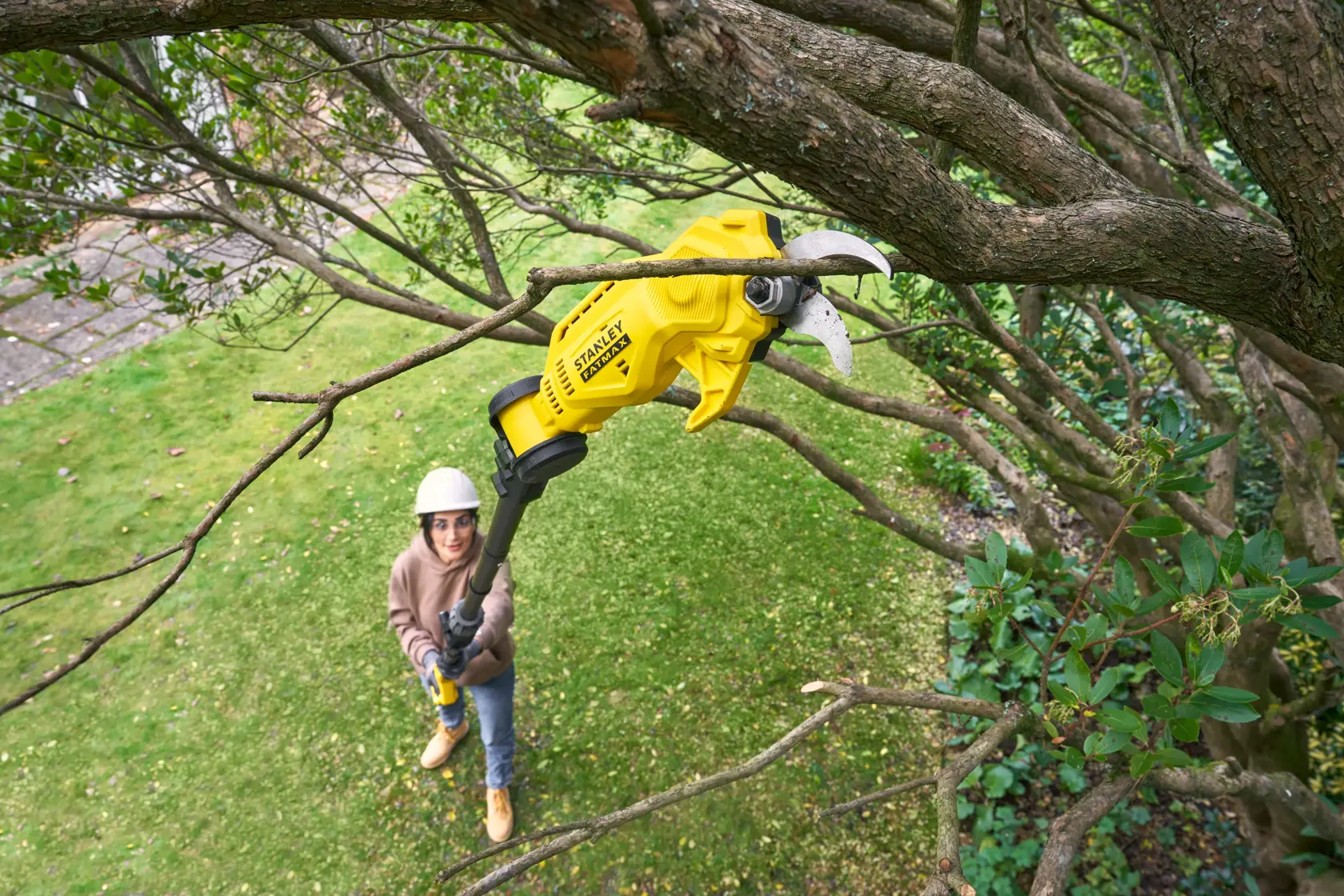STANLEY SFMCPP632D1 kabellose gelbe Stangenschere schneidet einen Ast im Außengarten.