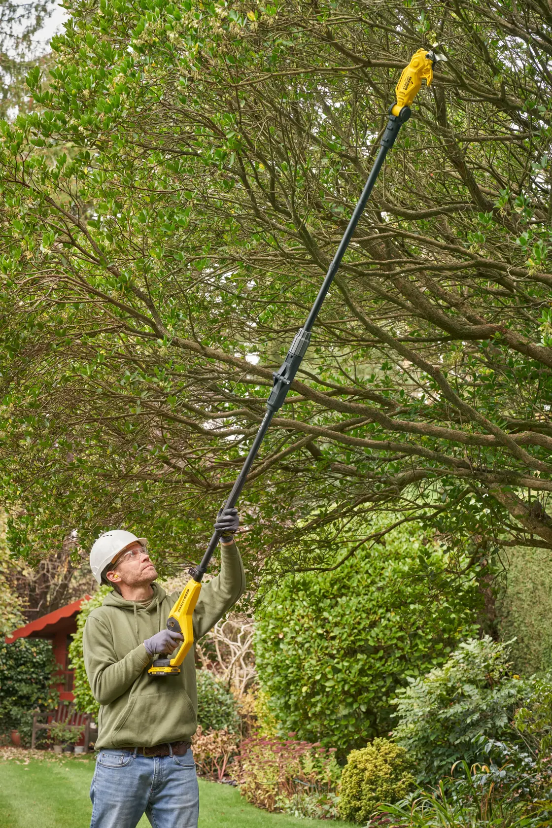 Foto der STANLEY SFMCPP632D1 Hochentaster beim Schneiden hoher Äste im Garten.
