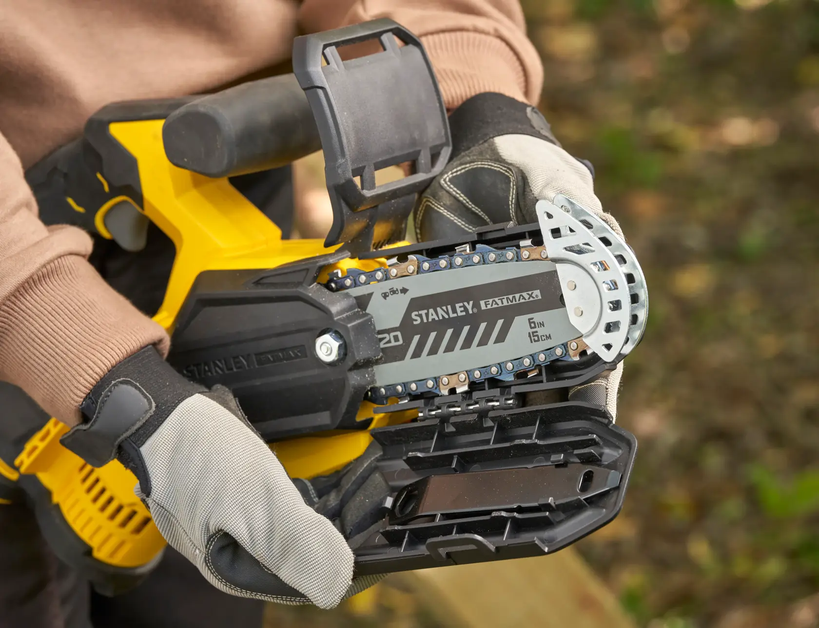 STANLEY SFMCPS415D1 FatMax Kettensäge Nahaufnahme, zeigt Schienenführung und Schutzhandschuhe im Freien.