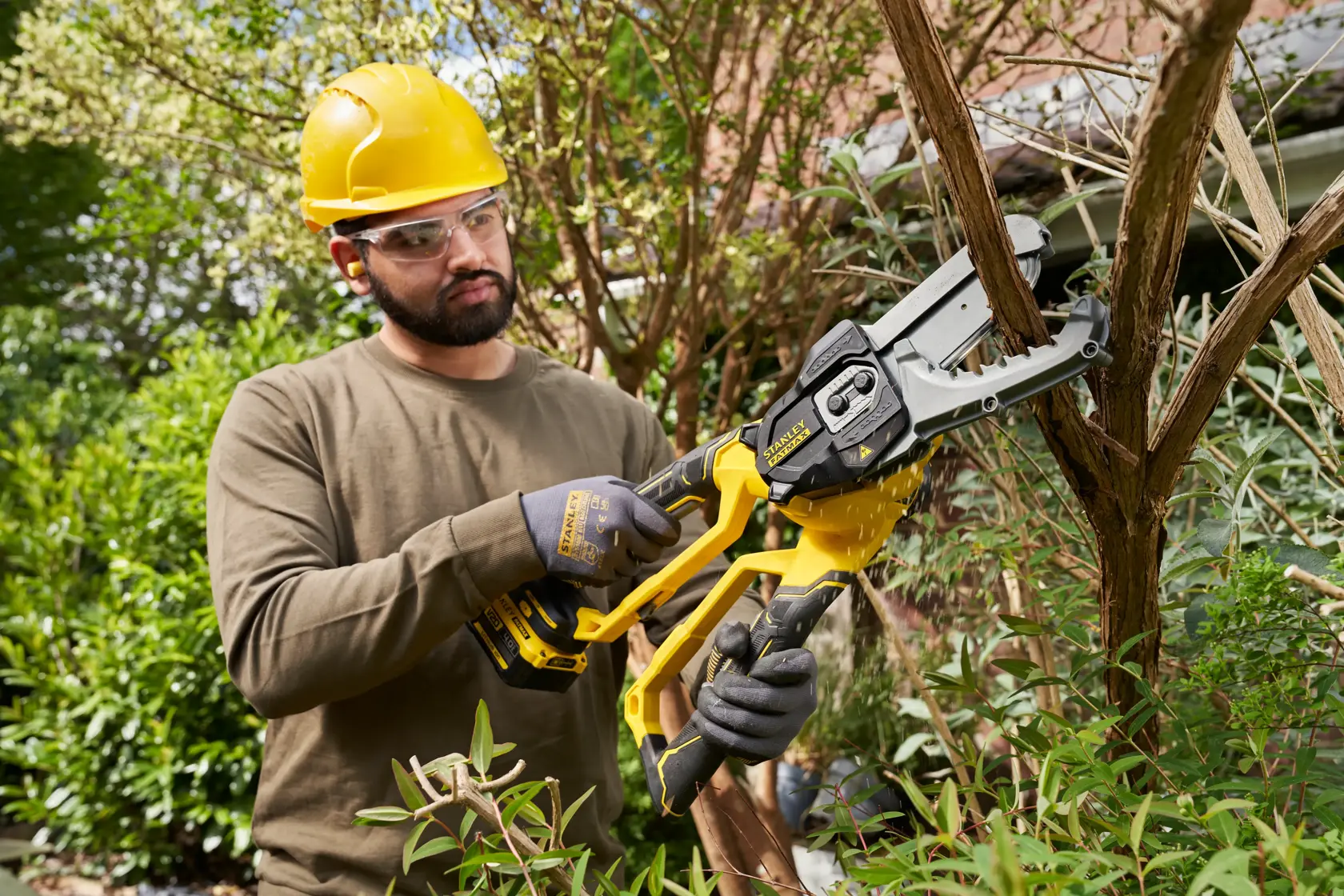 Photo of worker using STANLEY SFMCPS515M1 cordless chainsaw to cut tree branches in garden.