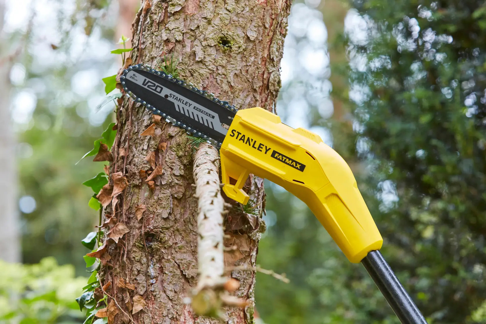 Photo of STANLEY SFMCPS620M1 pole saw cutting a tree branch, showing yellow body and black saw blade outdoors.