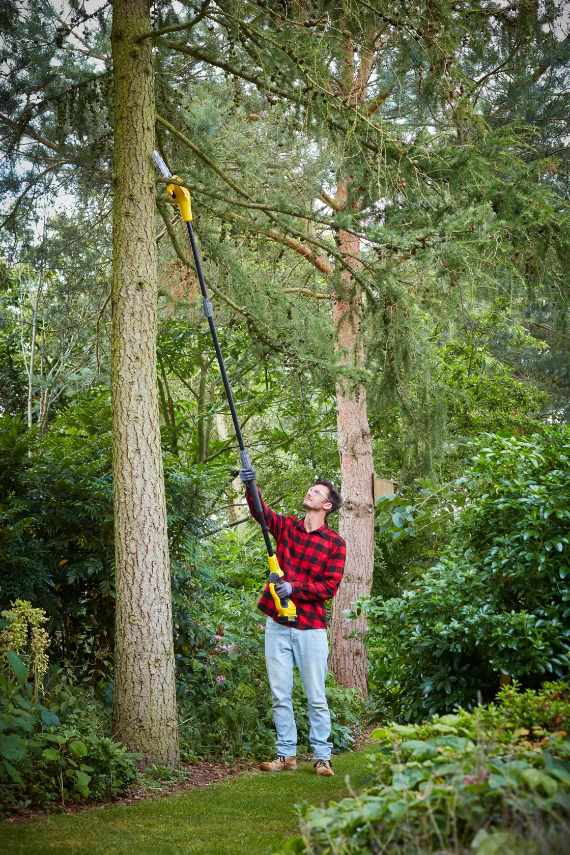 STANLEY SFMCPS620M1 pole saw used outdoors for pruning high tree branches in a garden.