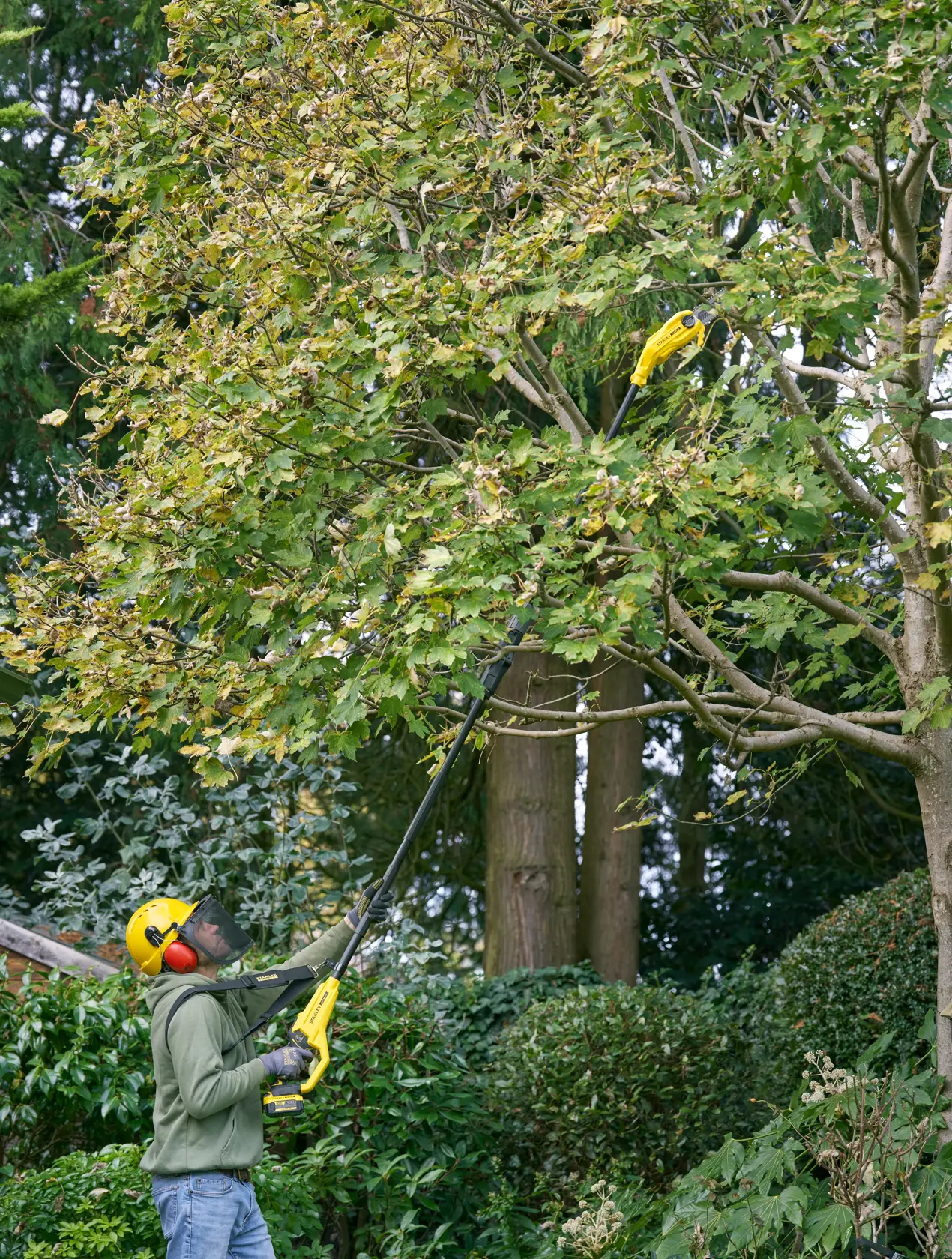 Foto einer Person, die Äste mit der STANLEY SFMCPS720B-XJ Astsäge in einem Garten schneidet.