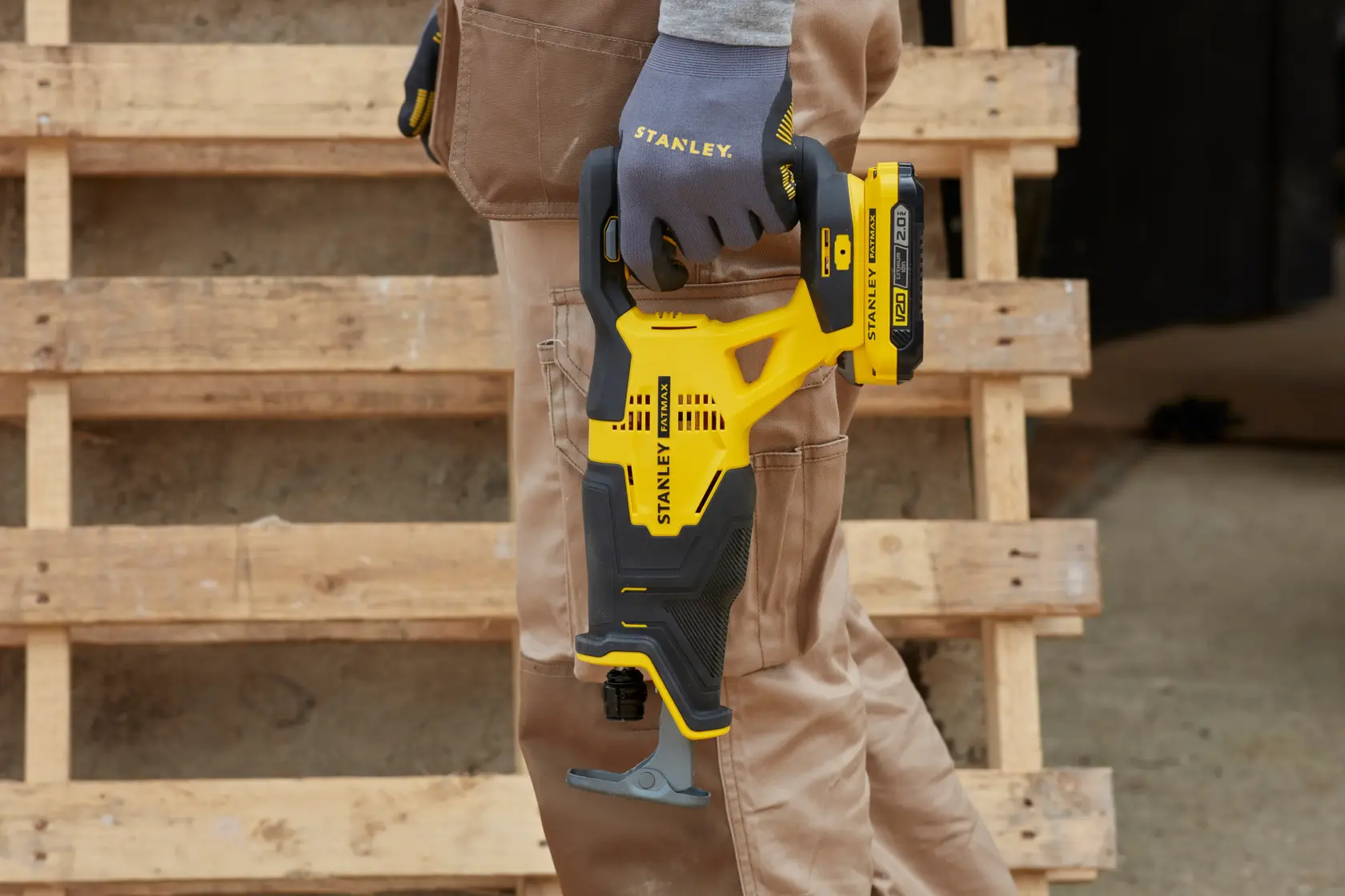 STANLEY SFMCS300D2K cordless reciprocating saw held by gloved hand, yellow and black design, outdoor setting.