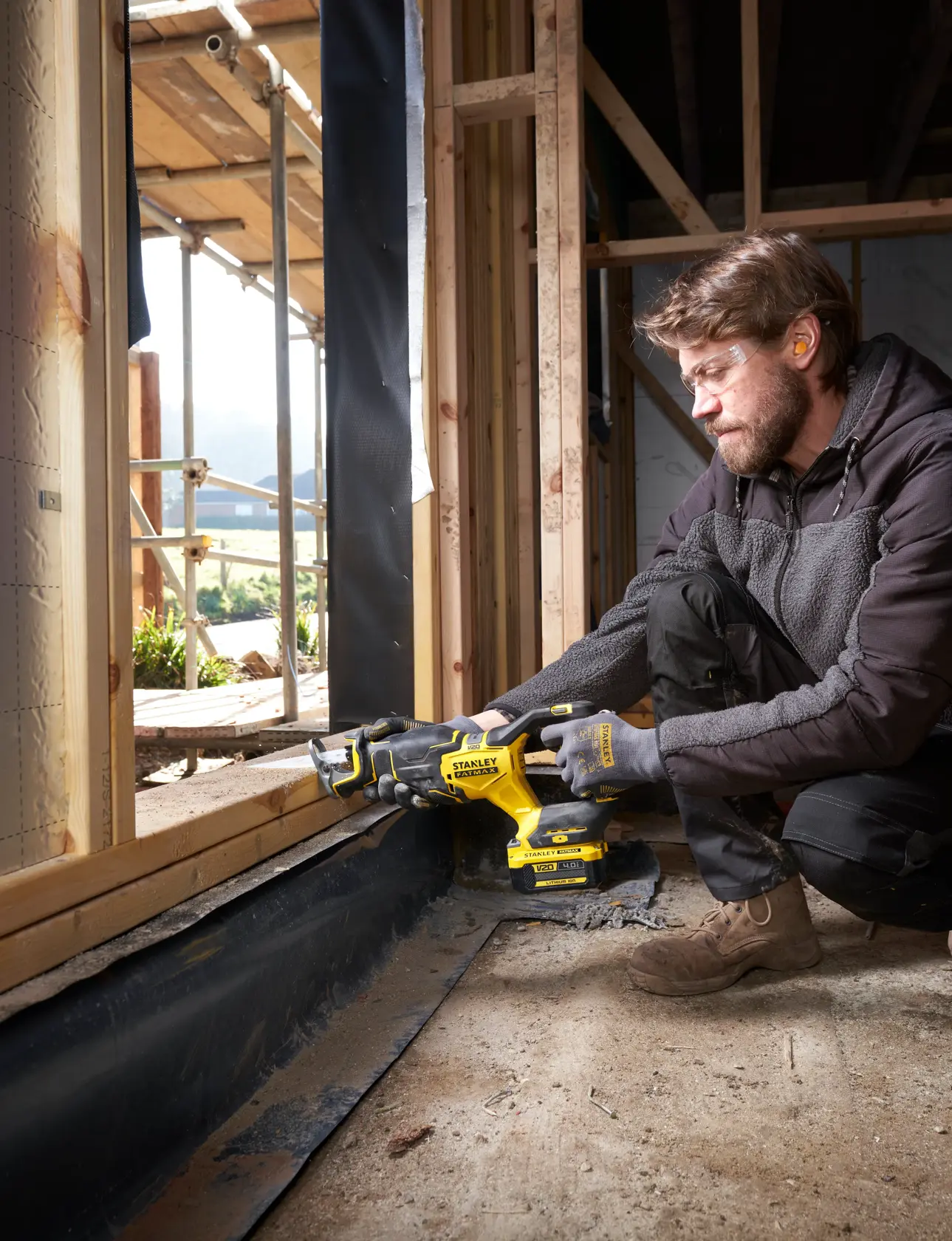 Photo of STANLEY SFMCS311B-XJ cordless reciprocating saw in use at a construction site, cutting wood near a window frame.