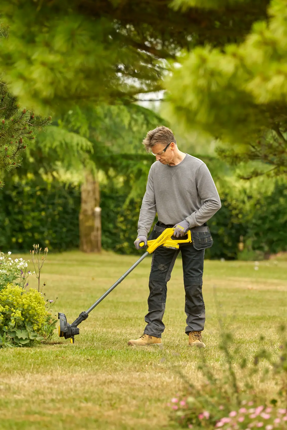 STANLEY SFMCST925B Rasentrimmer von einer Person im Garten benutzt, seitliche Außenansicht.