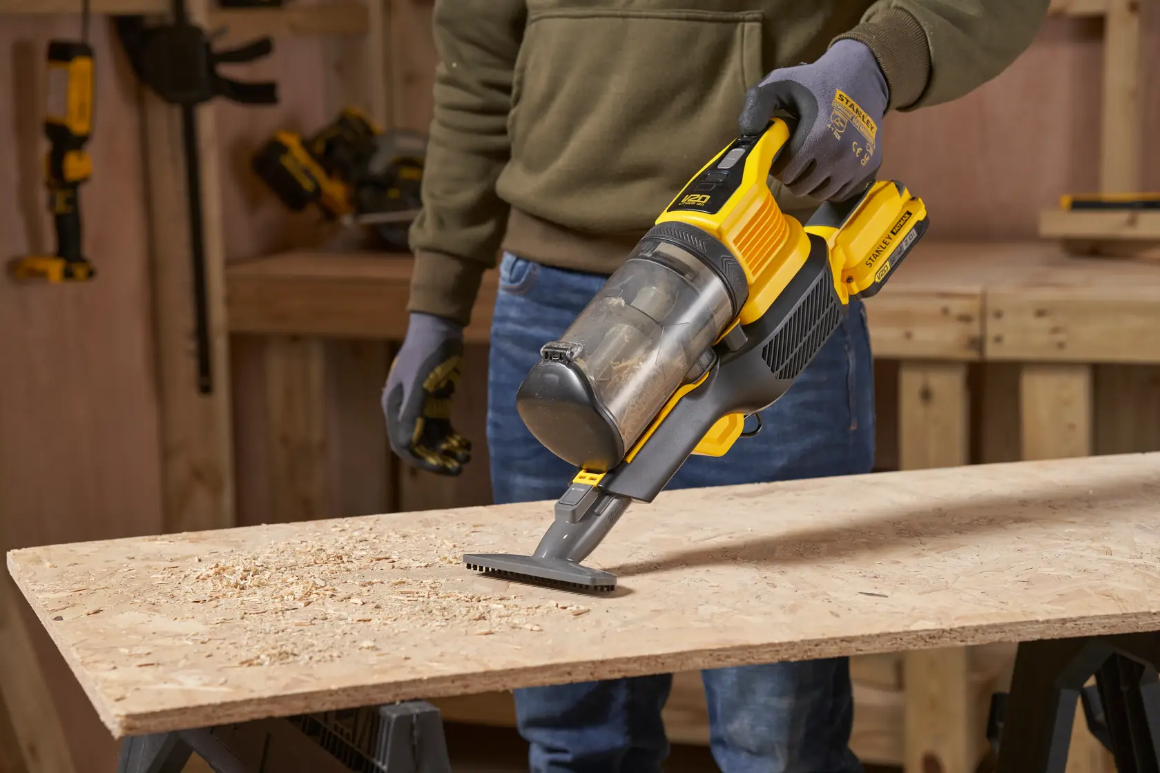 STANLEY SFMCVS001D1 Handstaubsauger reinigt Holzspäne auf einer Werkbank, Seitenansicht.