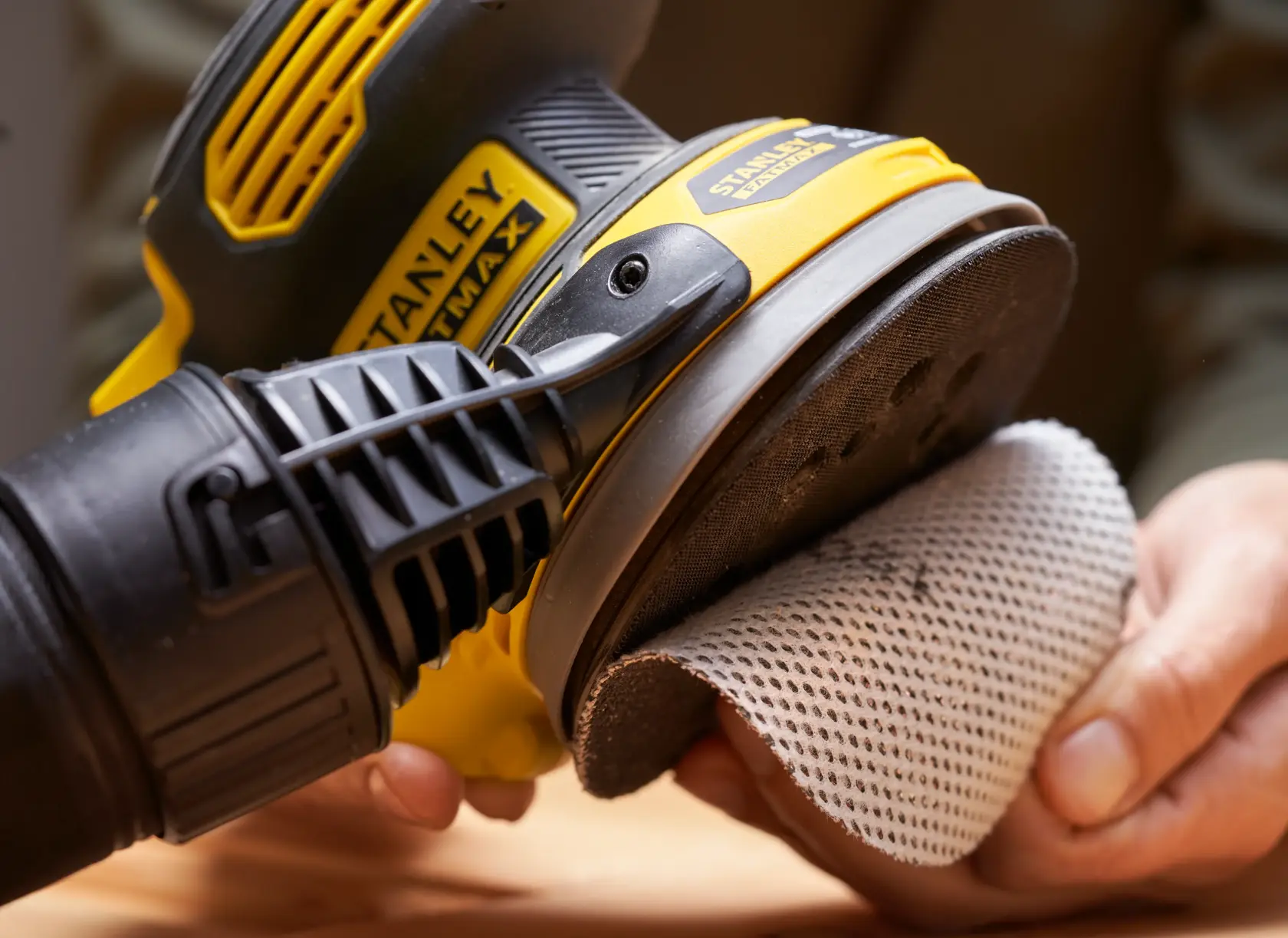 STANLEY SFMCW220B Schleifer in der Hand, Netz-Schleifpad wird angebracht, Nahaufnahme.
