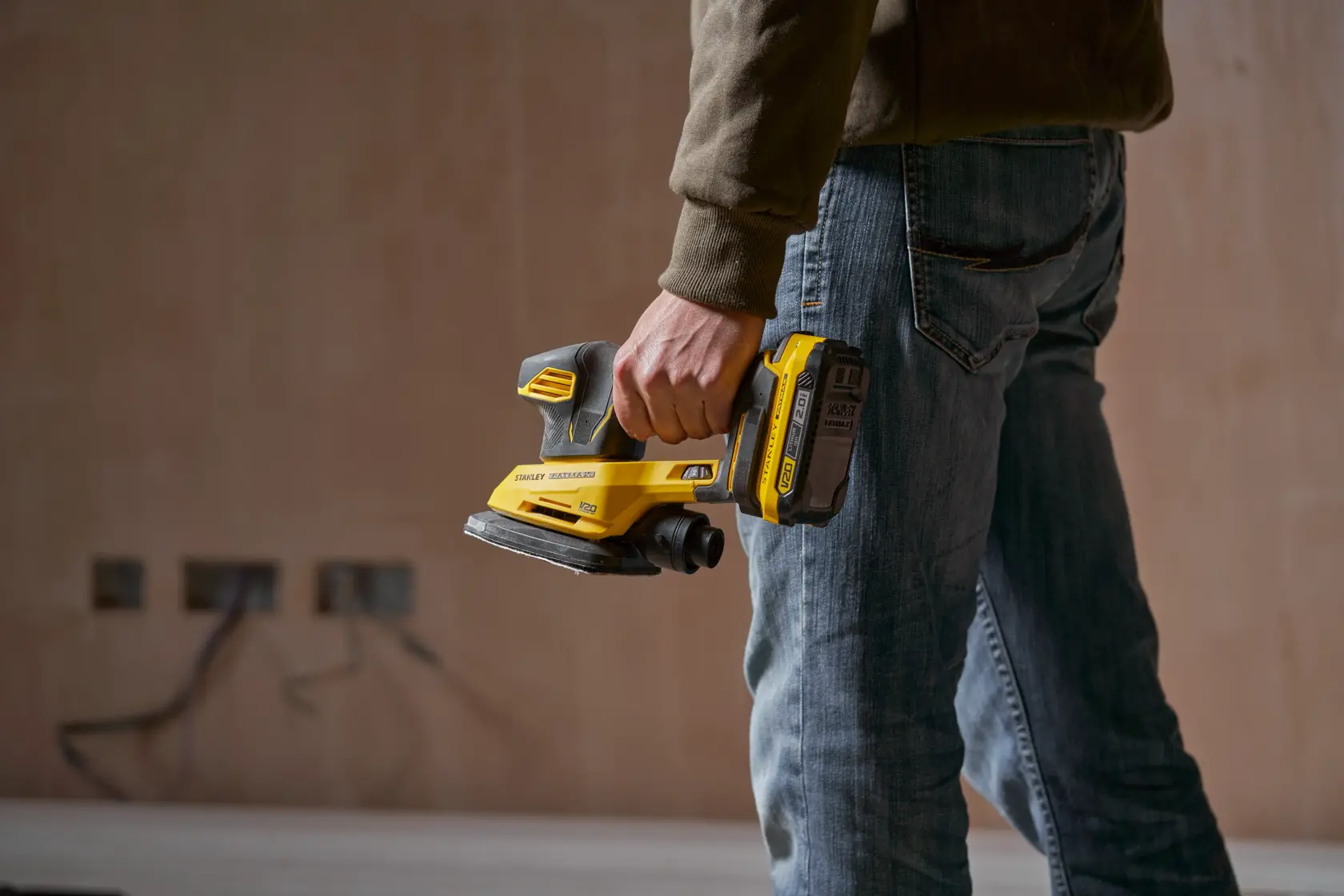 Foto der STANLEY SFMCW221B Akku-Schleifmaschine, gehalten von einer Person in Arbeitskleidung.