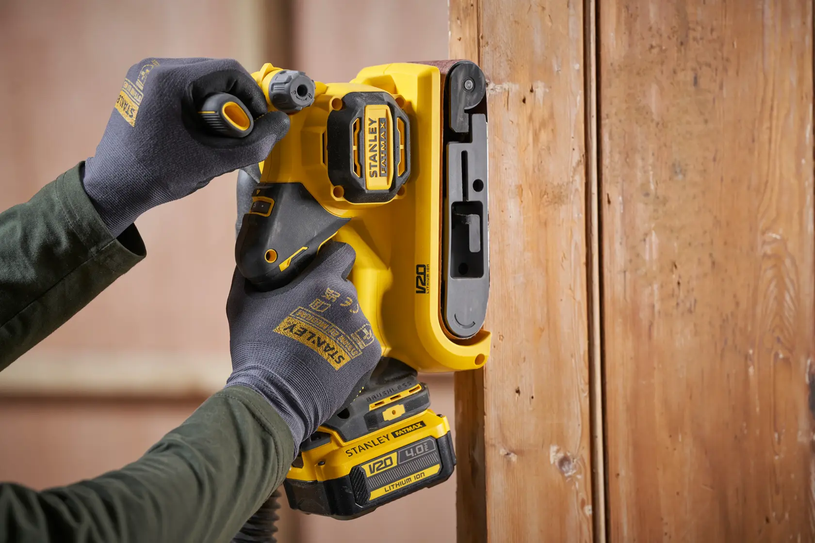 STANLEY SFMCW223B-XJ cordless sander in use on wood, close-up of yellow tool held by gloved hands.