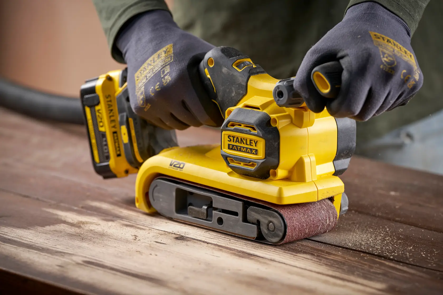 Stanley SFMCW223B-XJ cordless belt sander used on wood, close-up angle, yellow and black design.
