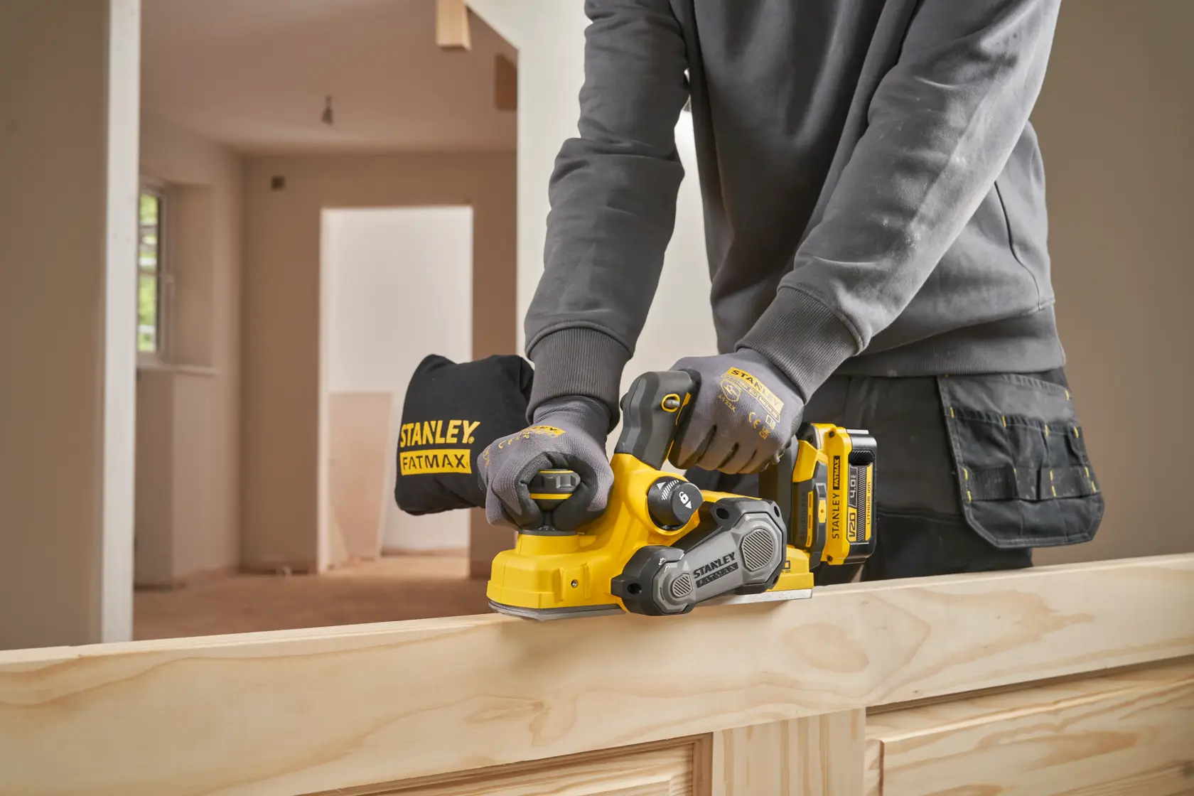 Stanley SFMCW300B kabelloser Hobel im Einsatz an Holz, Seitenansicht, Arbeiter mit Handschuhen.