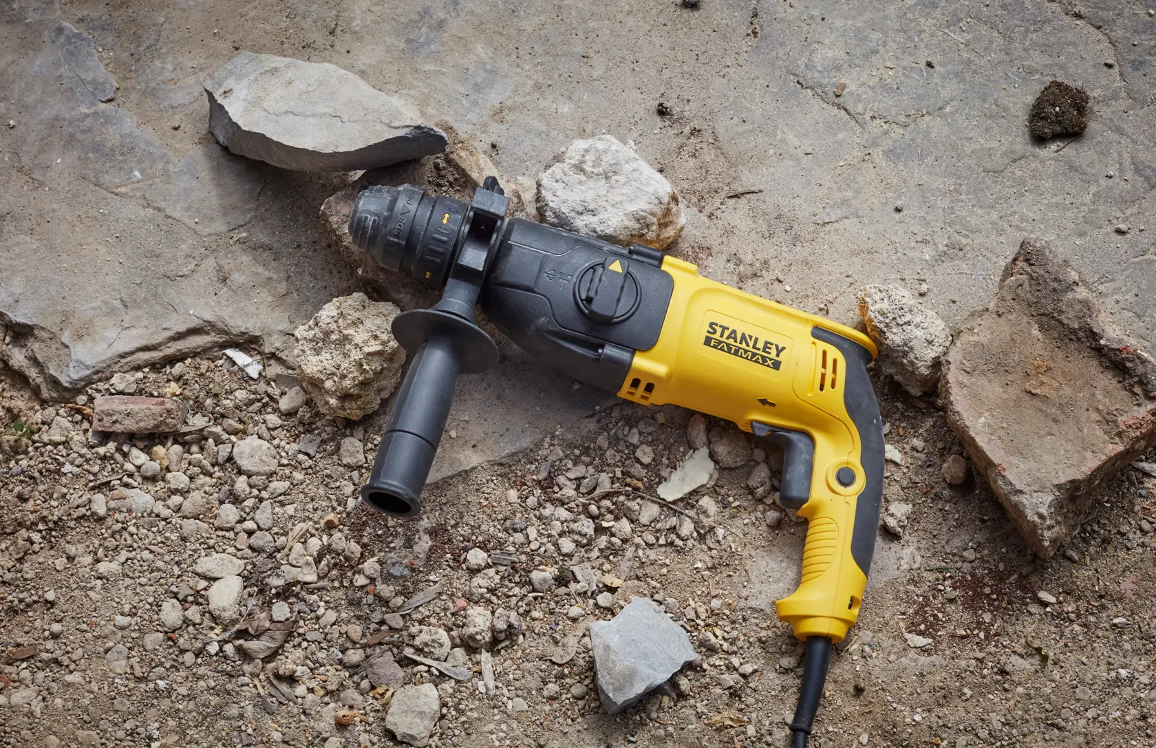 STANLEY SFMEH210K-QS kabelgebundene Schlagbohrmaschine in Gelb und Schwarz auf steinigem Boden.