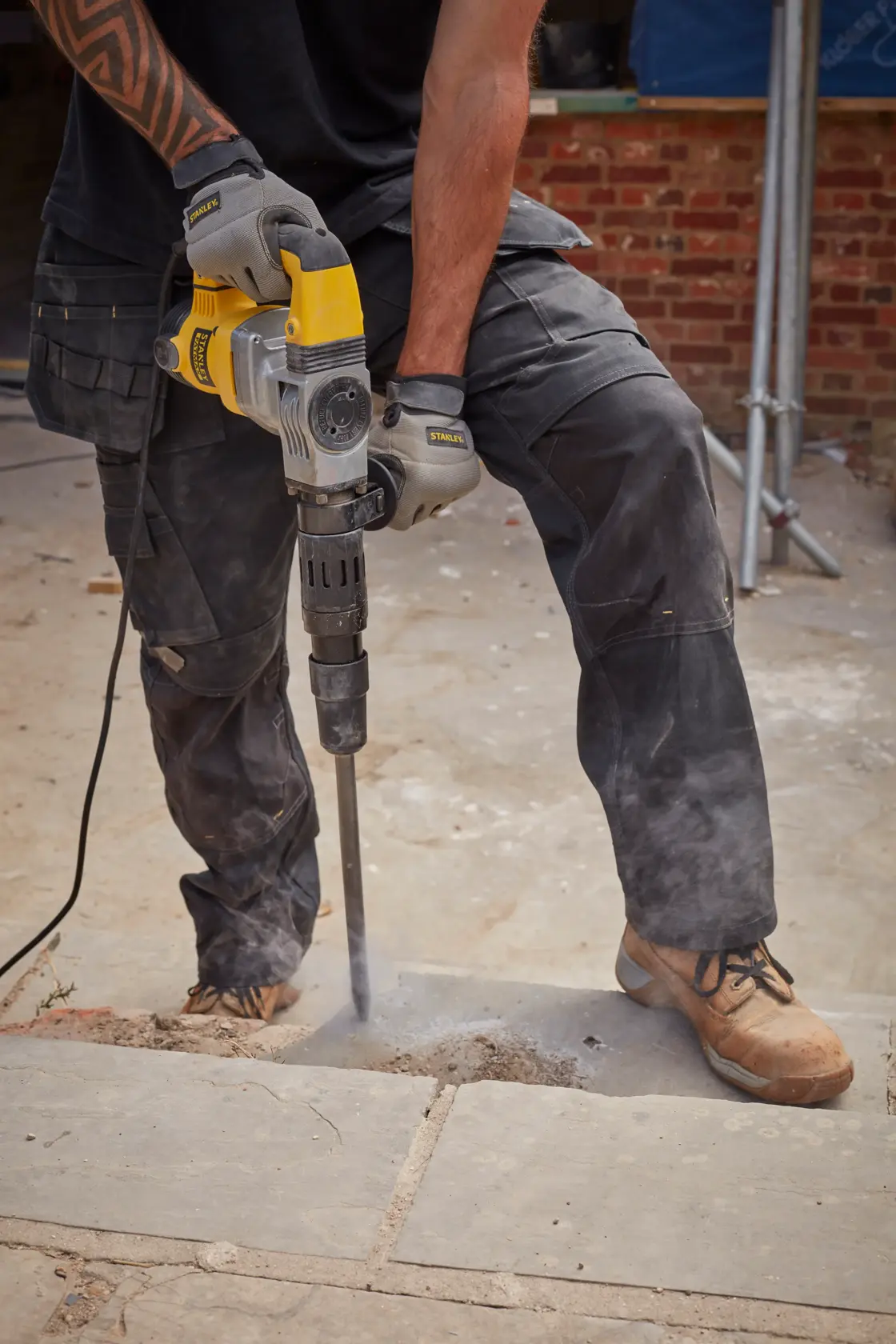 Stanley SFMEH220K-QS demolition hammer in use, breaking concrete outdoors, close-up of tool and worker's hands.